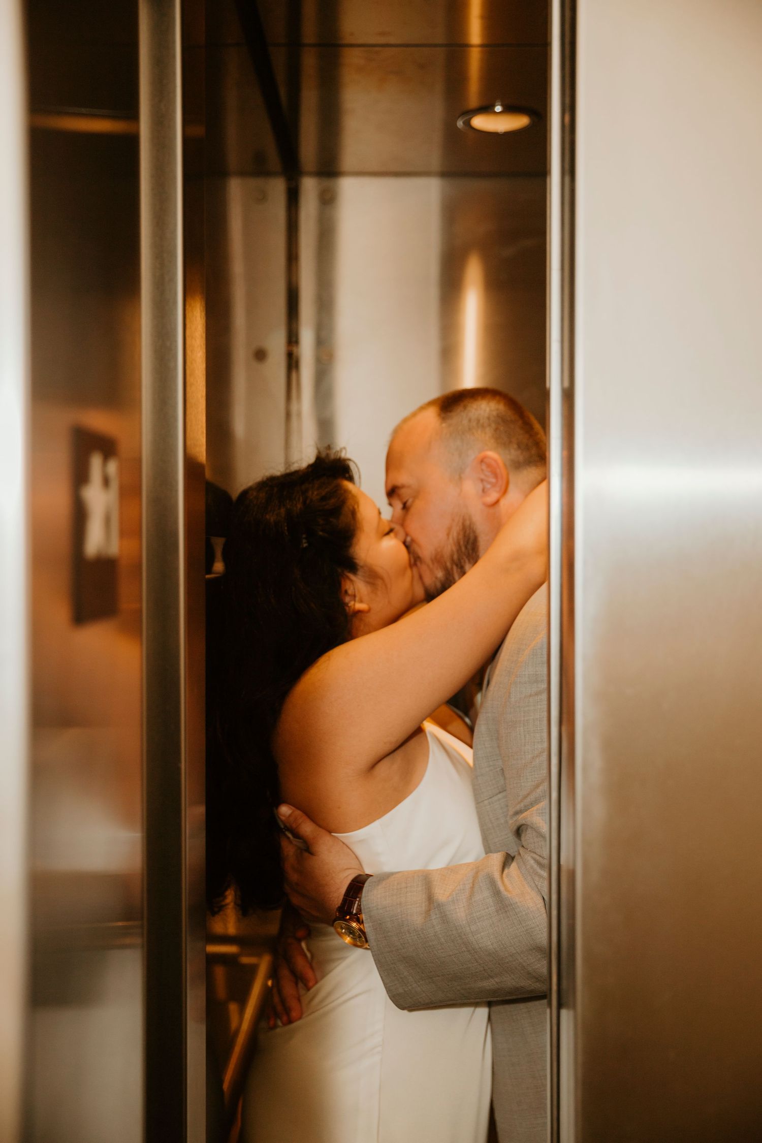 A romantic couple embraces and kisses in a softly lit hallway with a warm atmospheric glow.