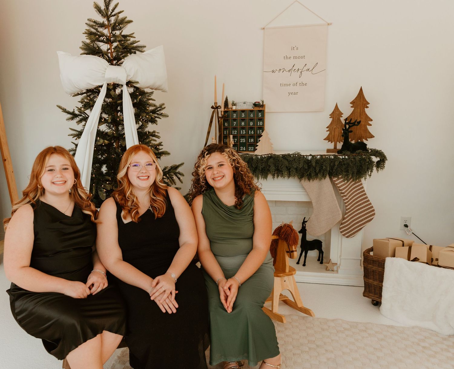 A group of people in black and green dresses sit together on a white couch during a festive holiday gathering.