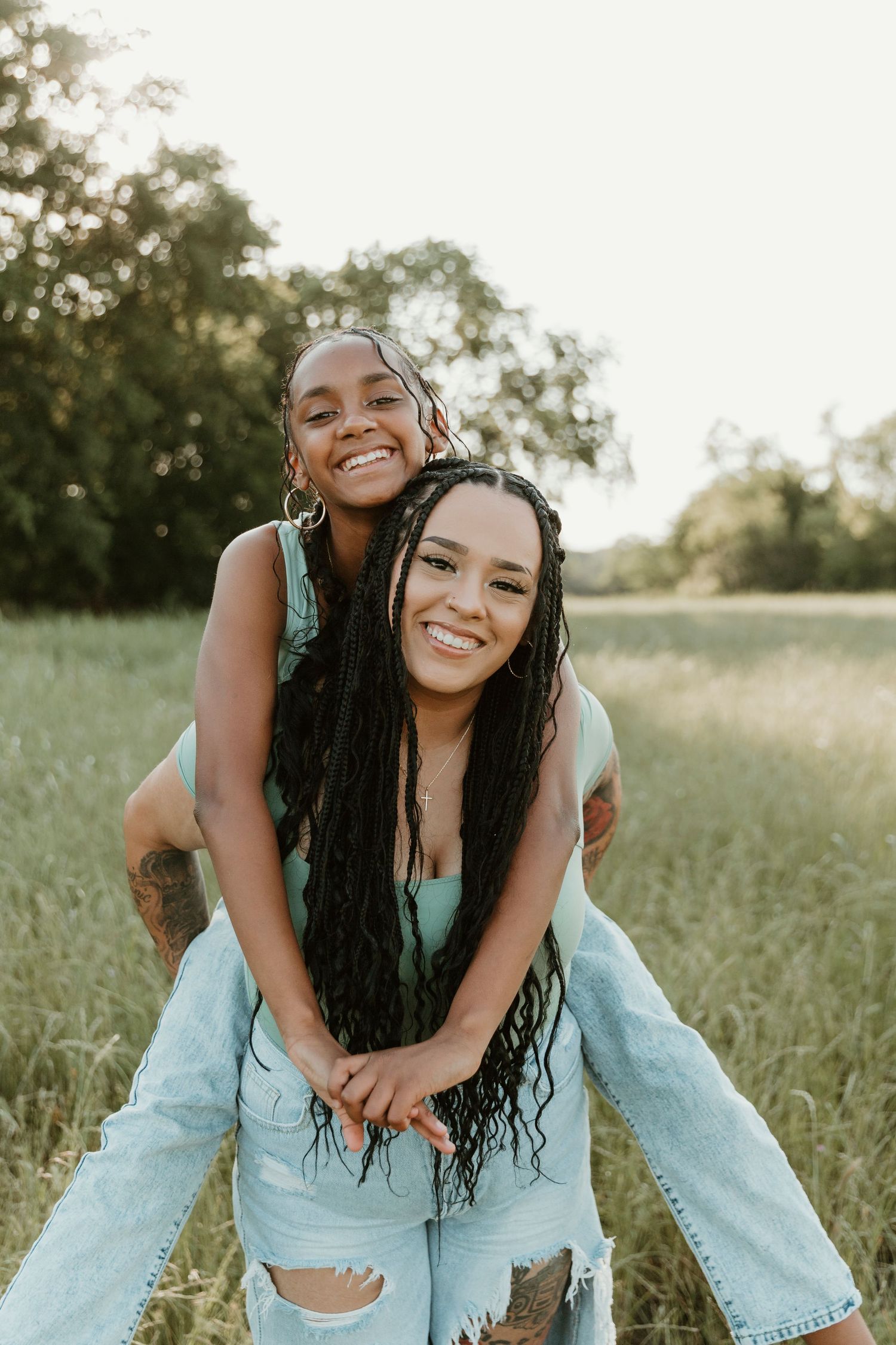 Friends share a playful piggyback ride in a sunlit meadow wearing matching outfits.
