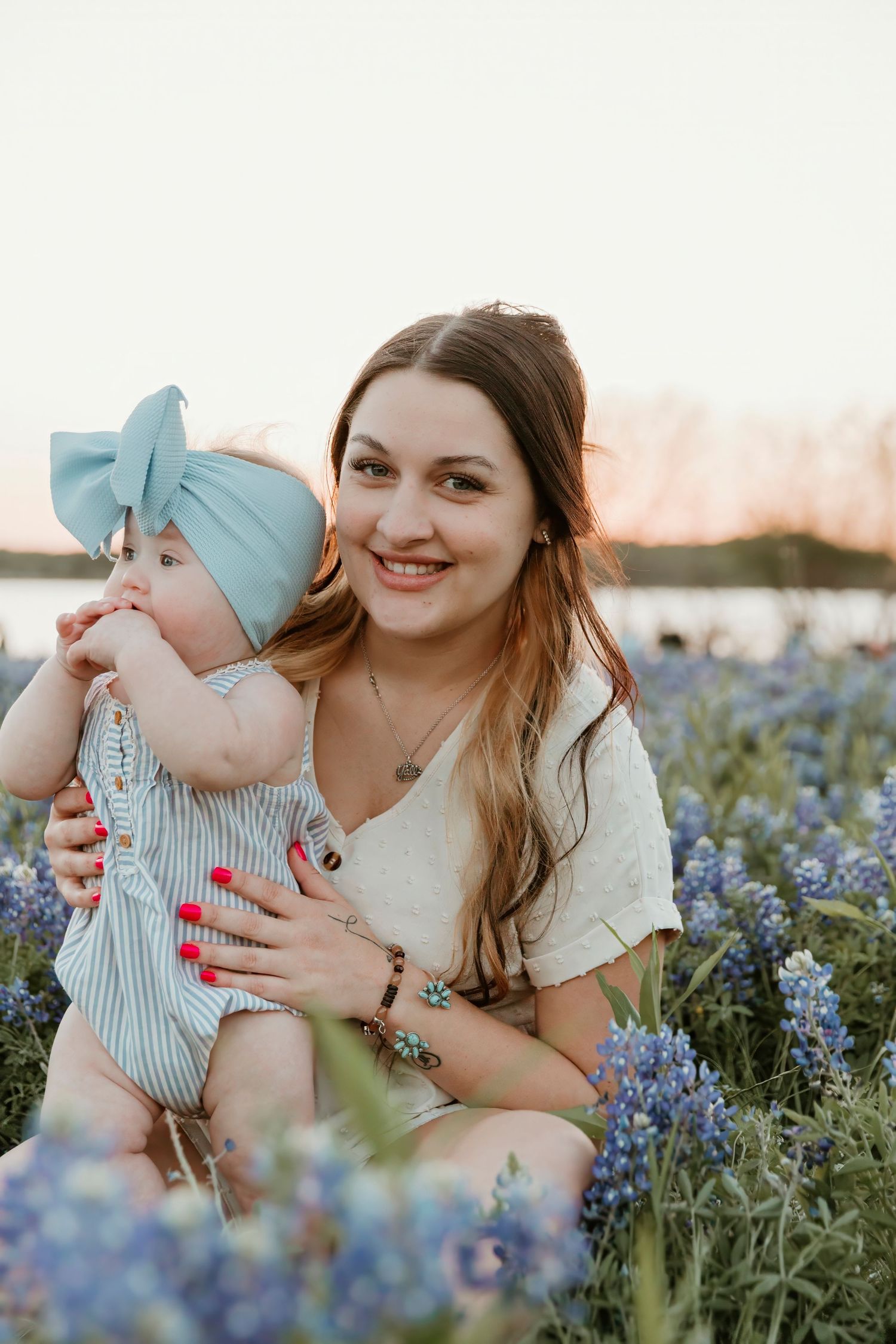 Mother and baby sharing loving moments while sitting among blooming bluebonnet flowers.