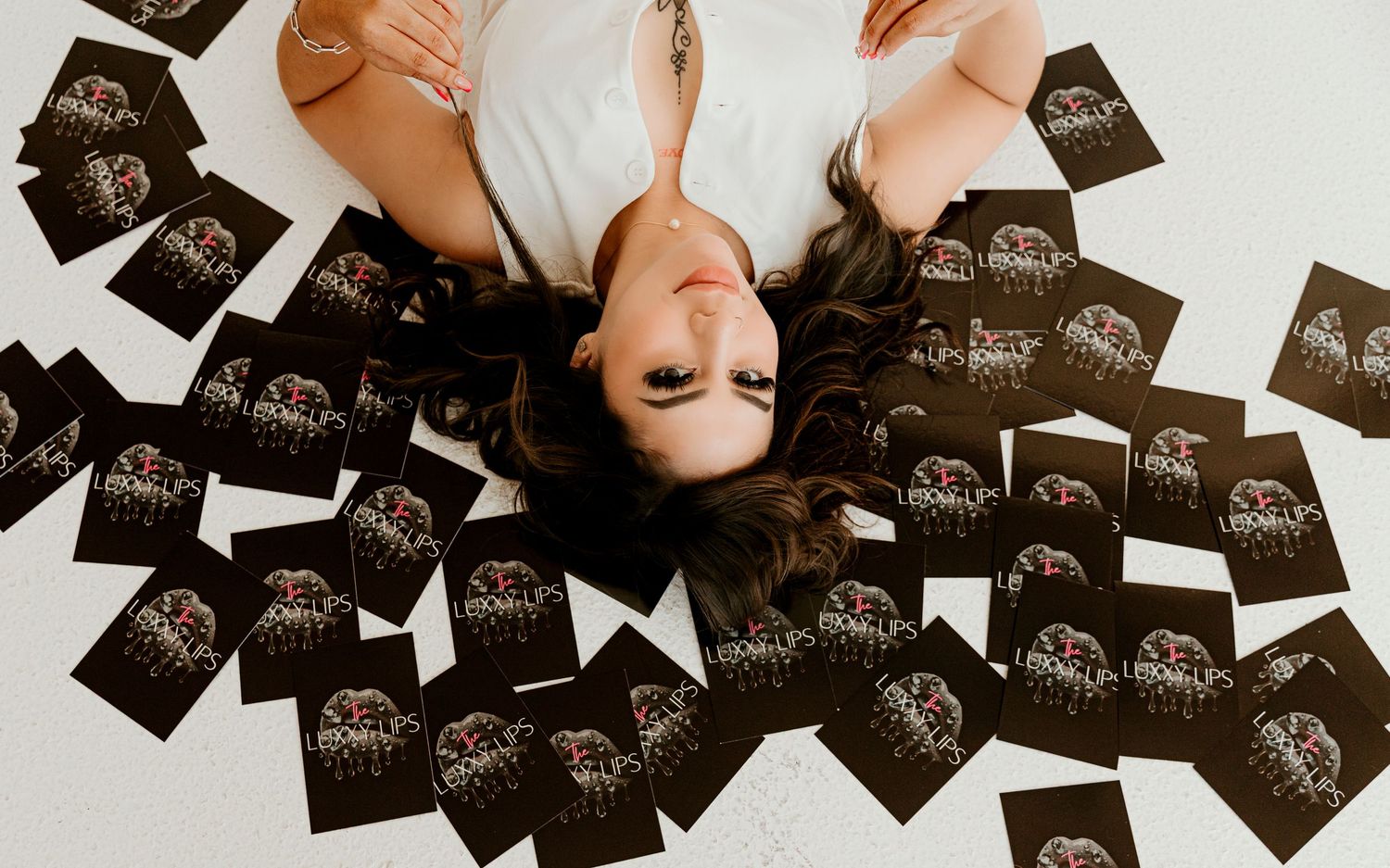 Artistic overhead shot of person lying among scattered black cards on white floor.