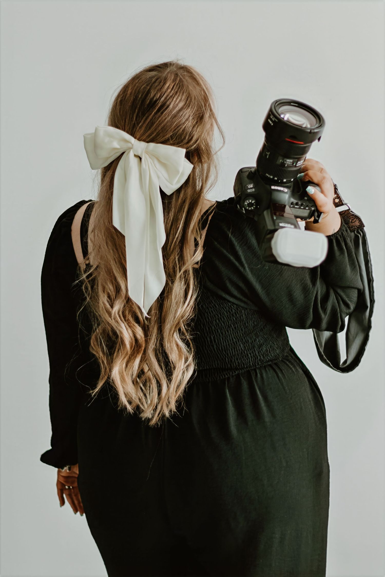Back view of photographer with white hair bow and long wavy hair holding professional camera.