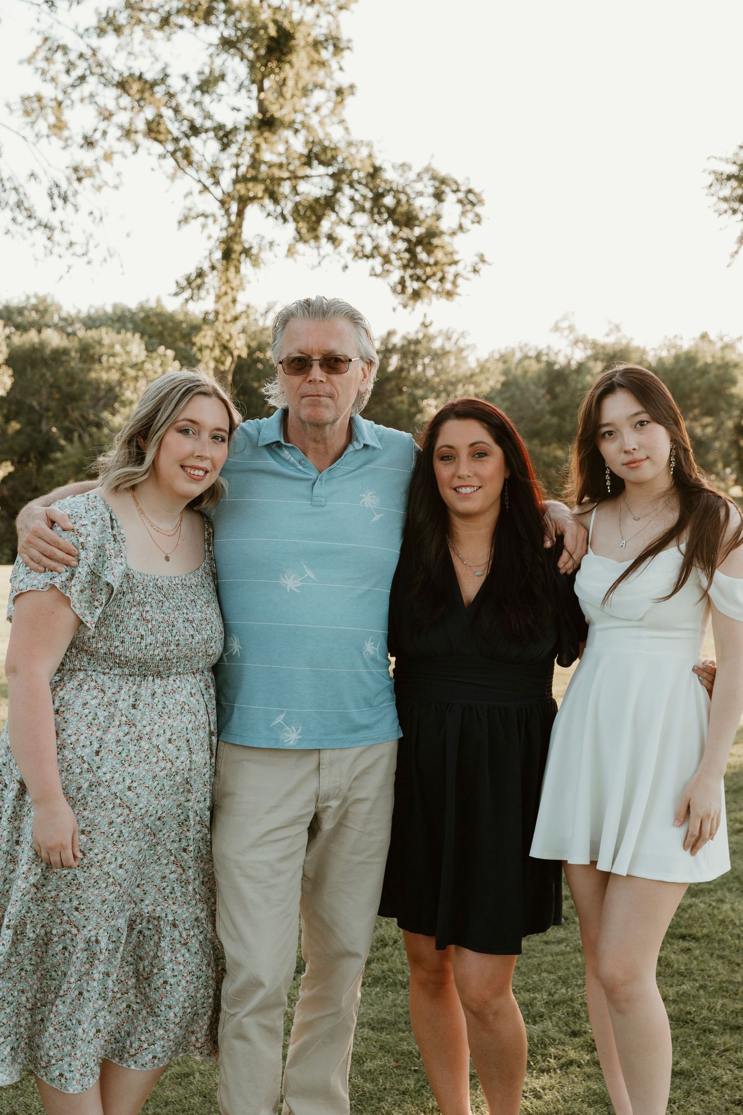Four people wearing casual attire pose together outdoors during golden hour.