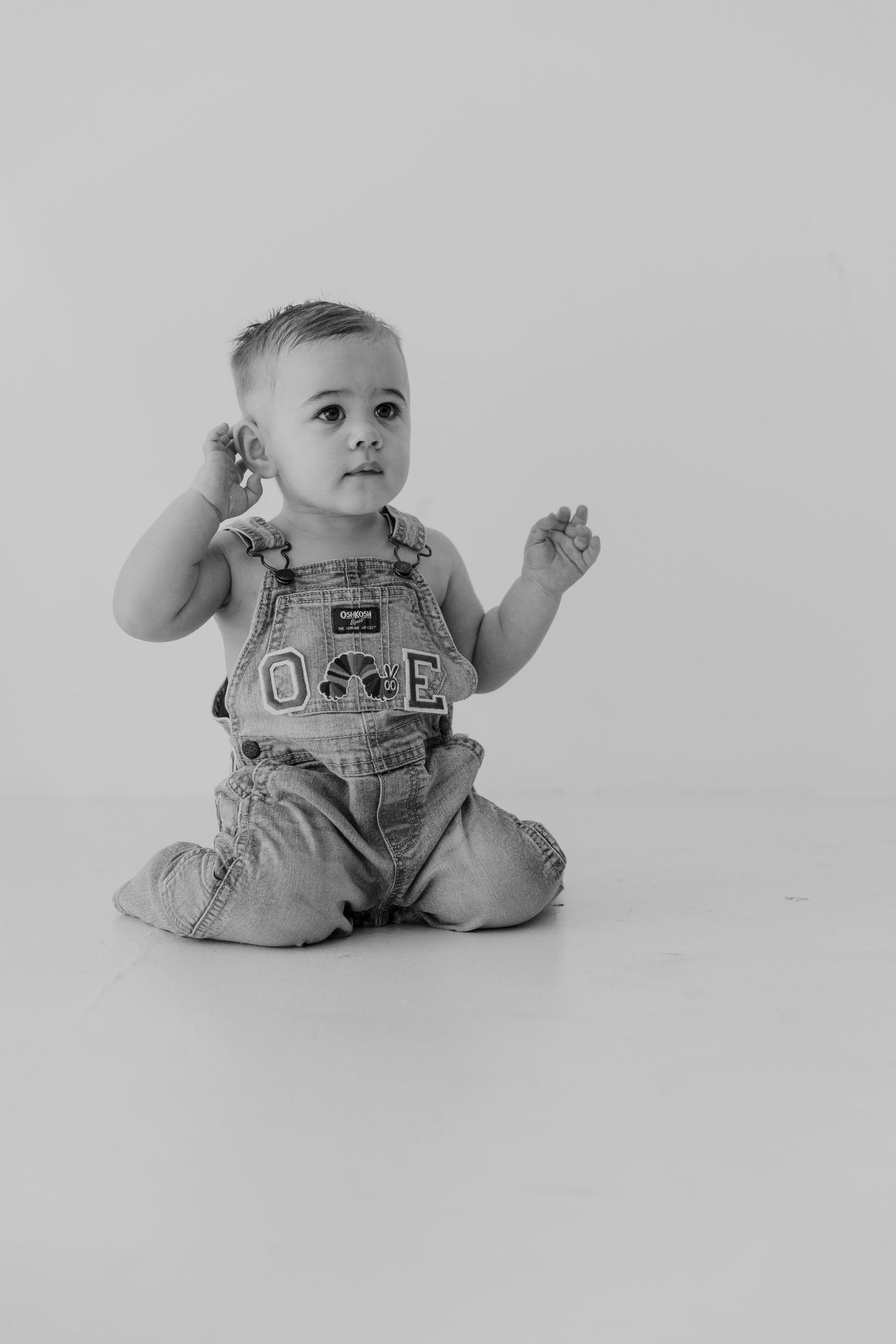 Black and white photo series of a baby wearing denim overalls sitting and moving in different playful poses.