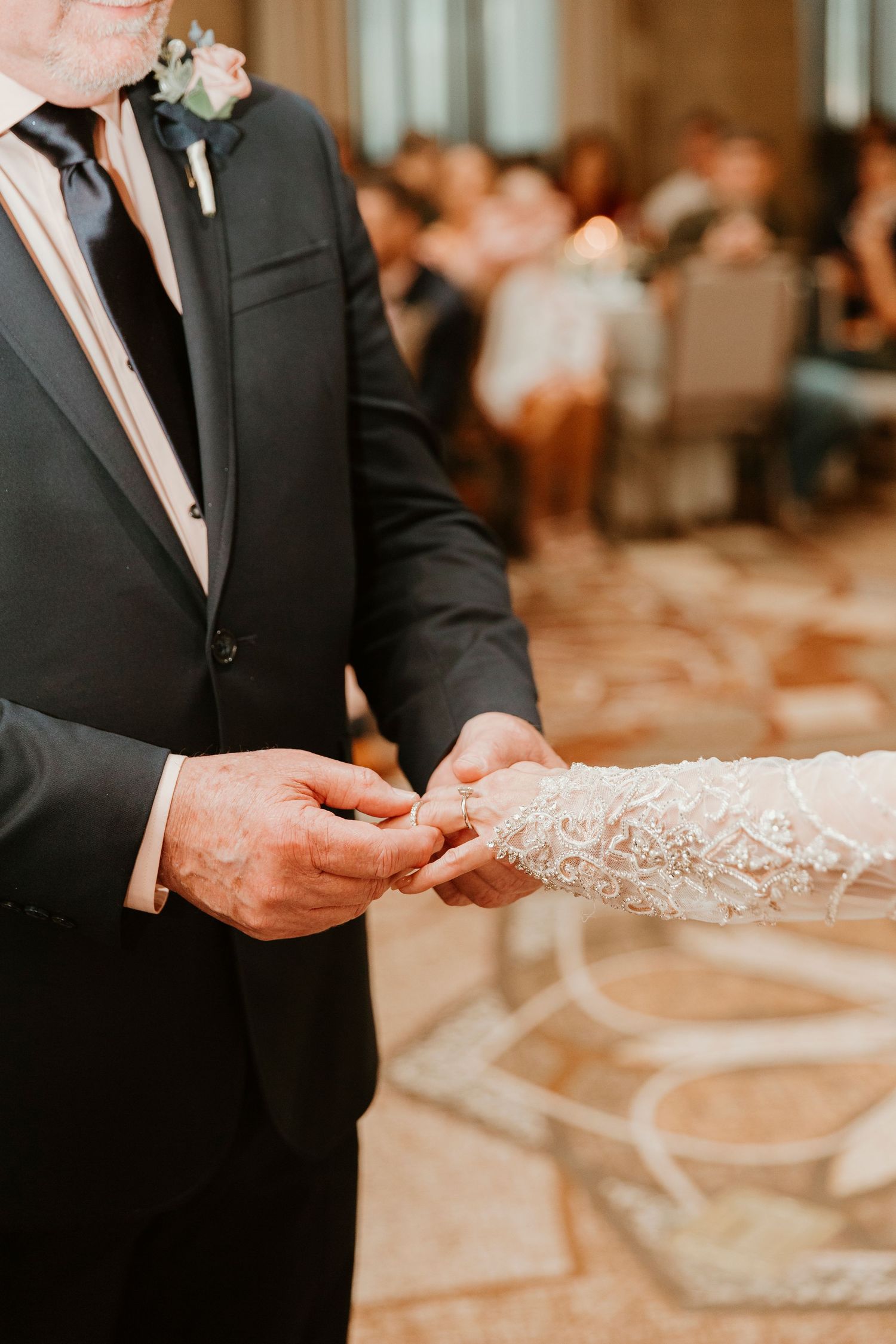 Closeup of groom placing wedding ring on bride's delicate lace-covered hand during indoor ceremony.