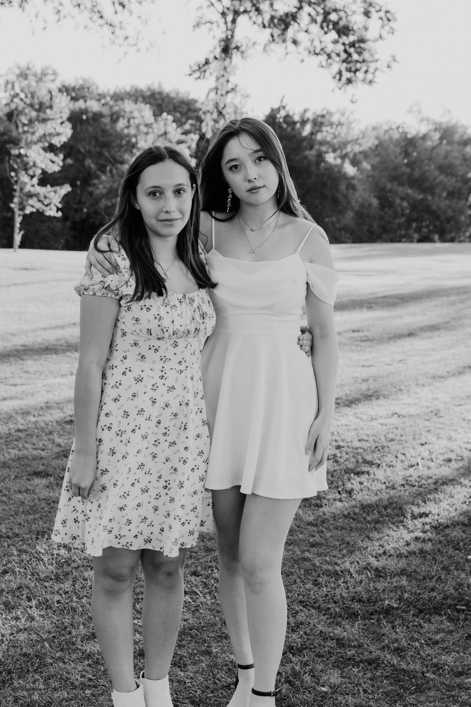 Two young people in summer dresses pose together in a black and white outdoor portrait.