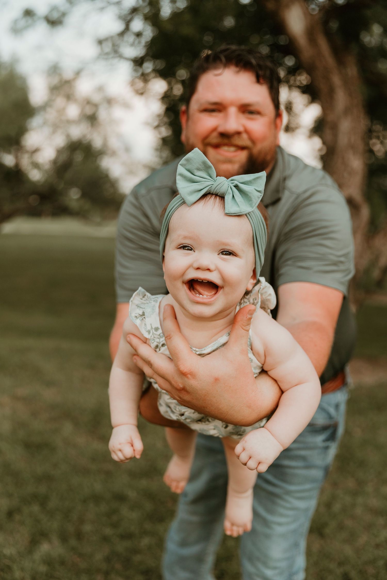A happy baby wearing a teal bow and floral romper shares a joyful moment outdoors.