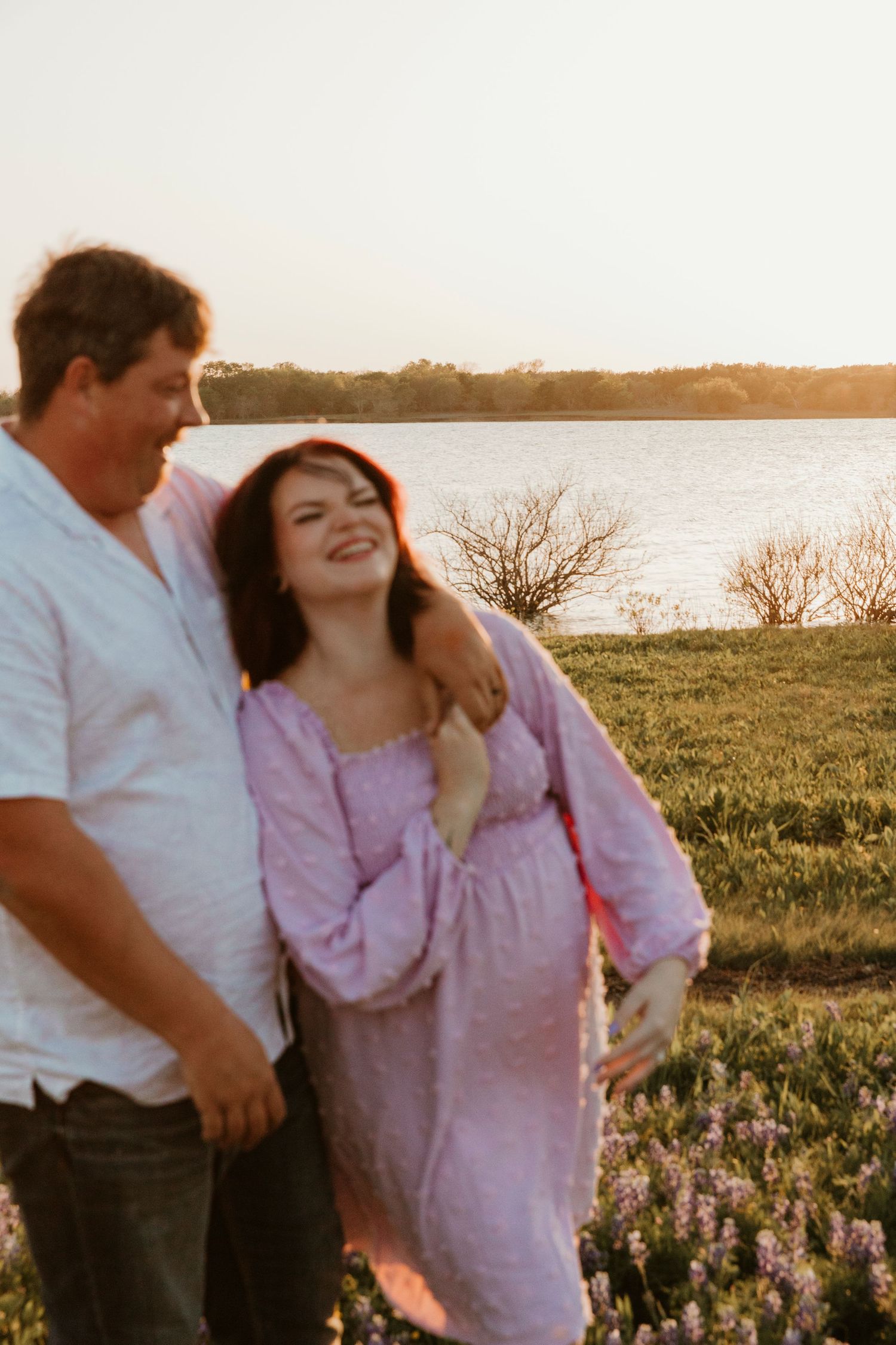 A joyful couple laughs together in a meadow with bluebonnets at golden hour.
