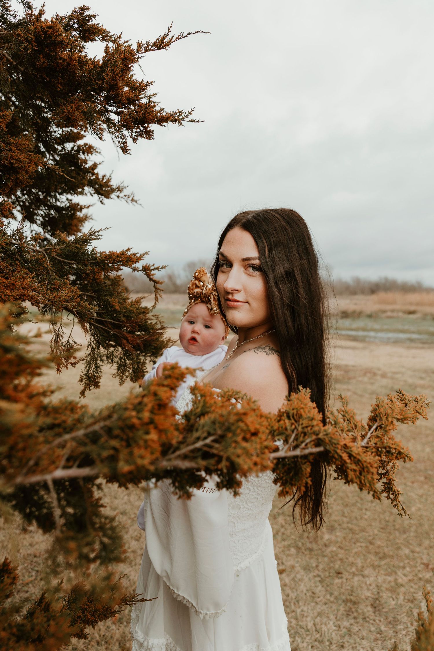 Artistic portrait among autumn branches wearing white dress in golden field.