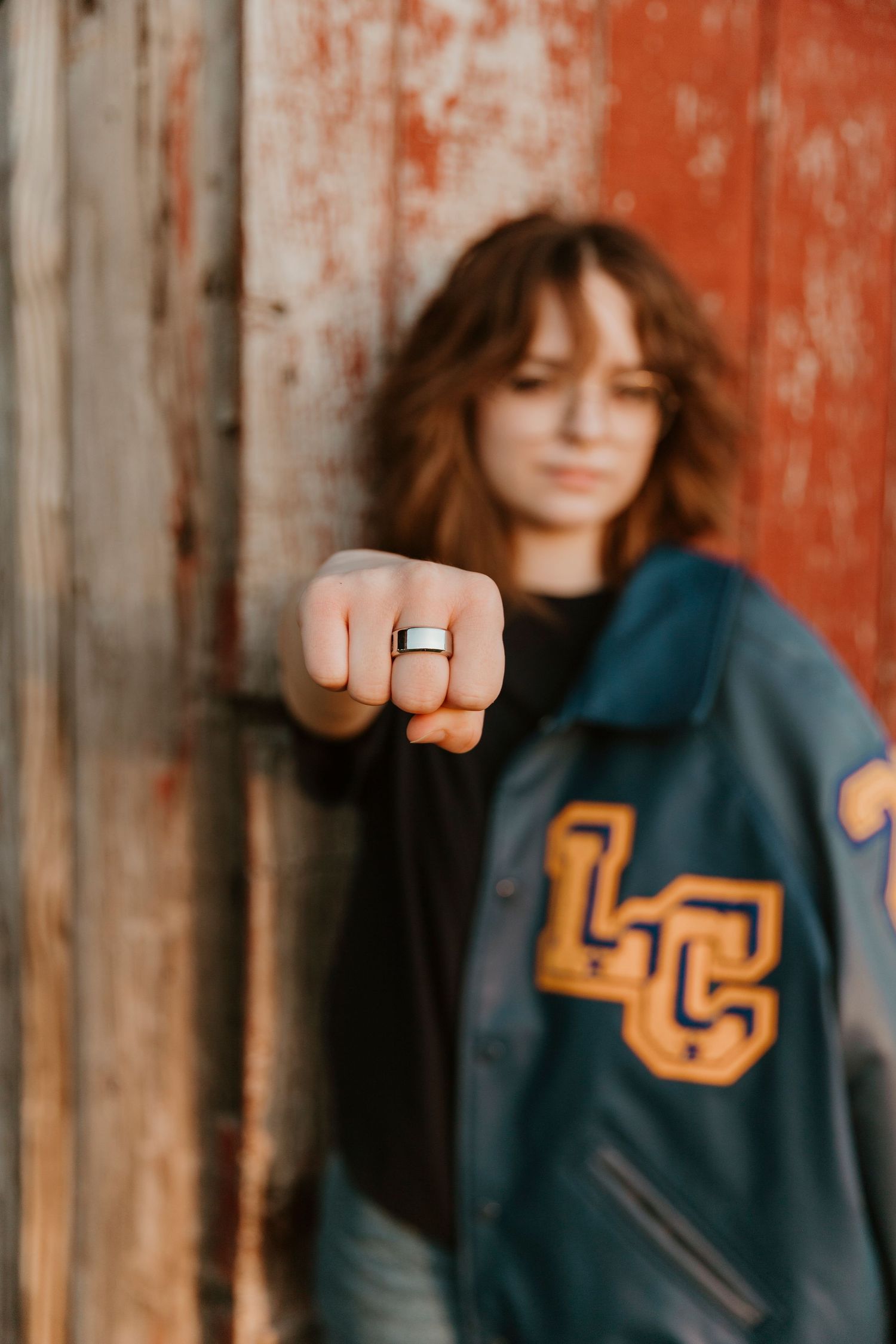 A vintage letterman jacket with yellow LC letters shown against a rustic red wooden wall.