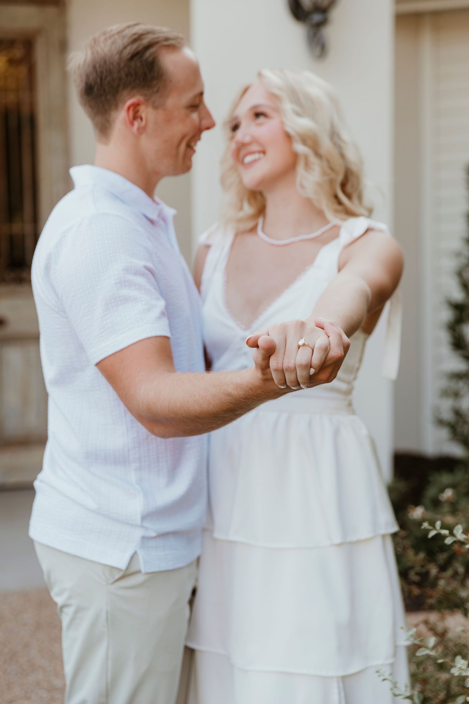 A couple in matching white attire dances and laughs together on a paved walkway.