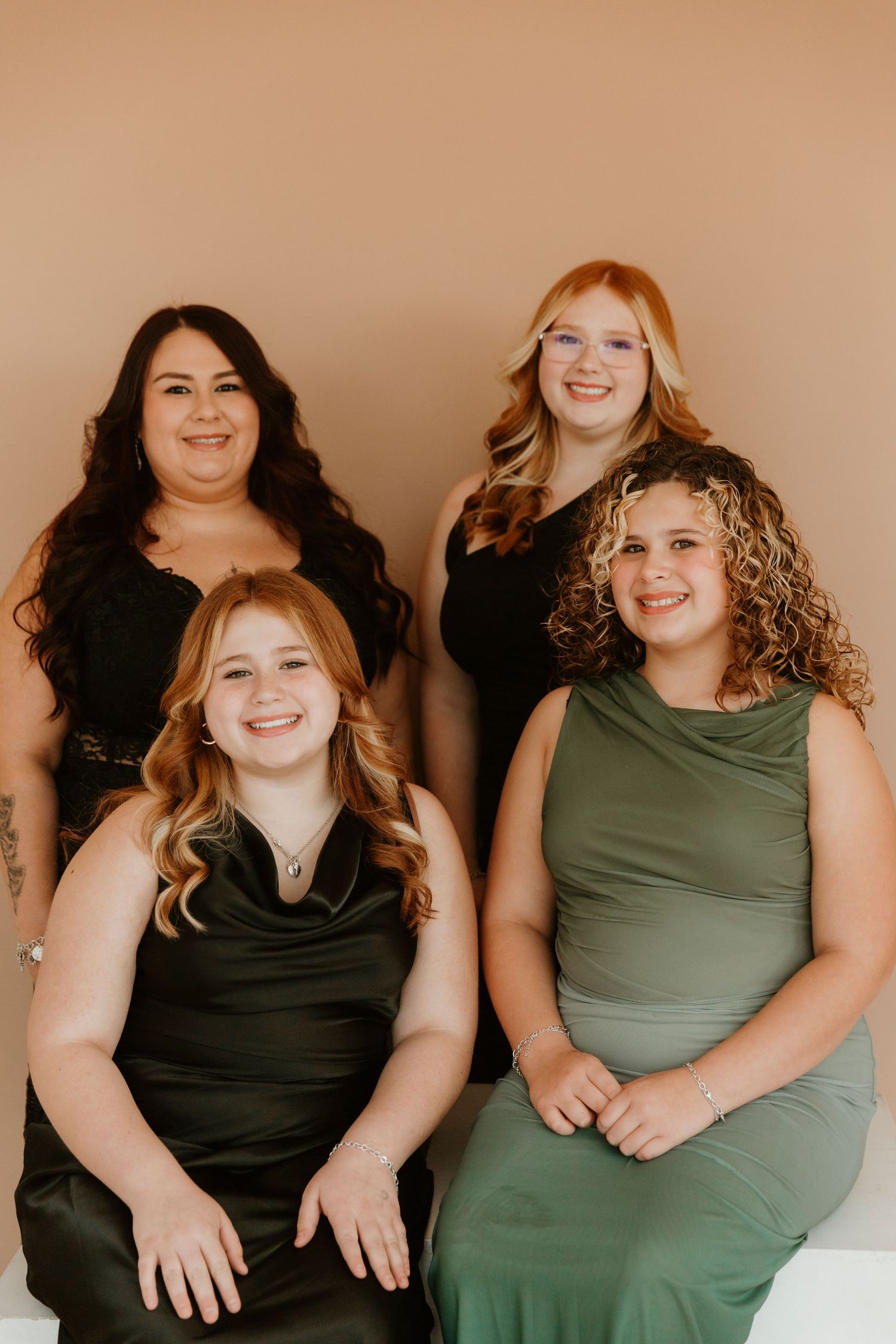 A series of four candid photos showing people in black and olive green tops sitting together against a beige backdrop.