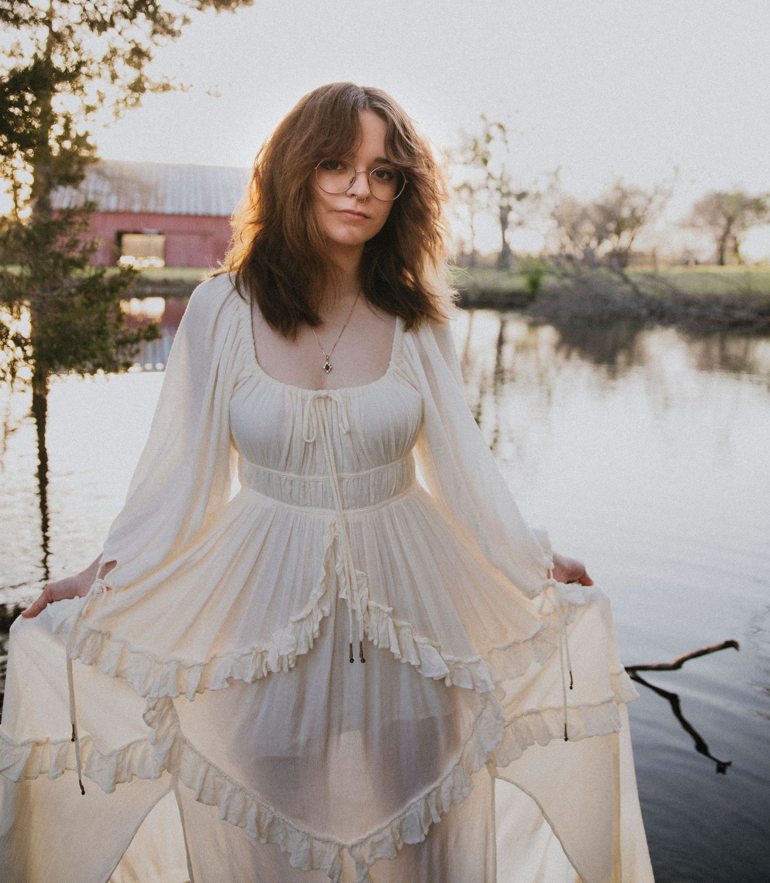 A flowing white vintage-style dress photographed by a tranquil pond at dusk.