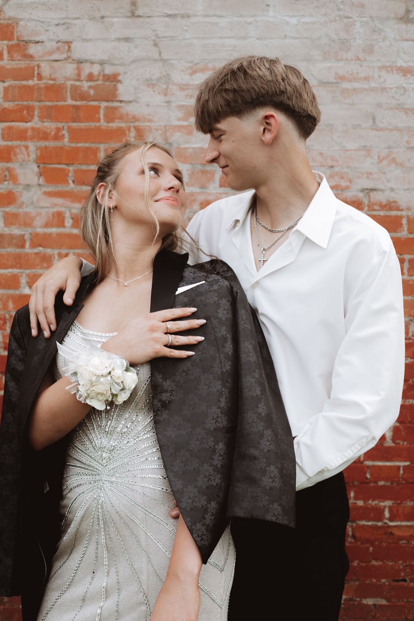 Couple in formal attire posing against rustic brick wall.