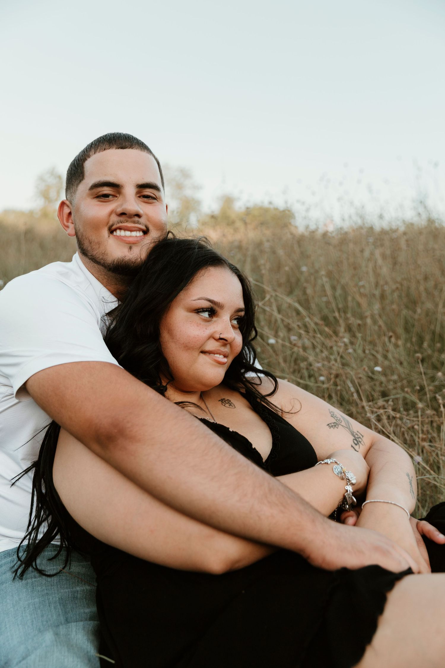 A loving couple embraces while sitting in a golden grassy field during sunset.