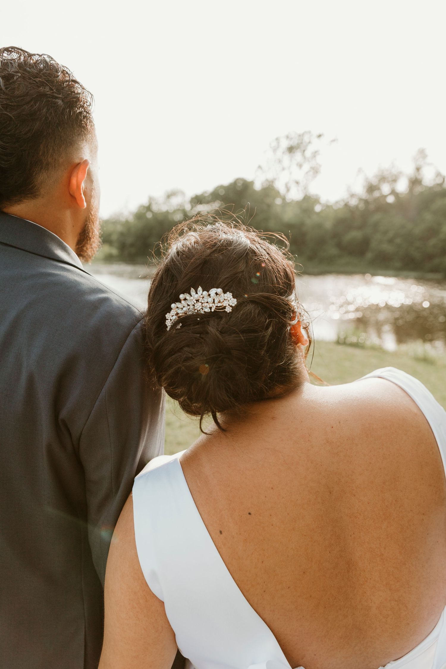 Back view of couple in wedding attire looking at sunset with ornate hair accessory detail.