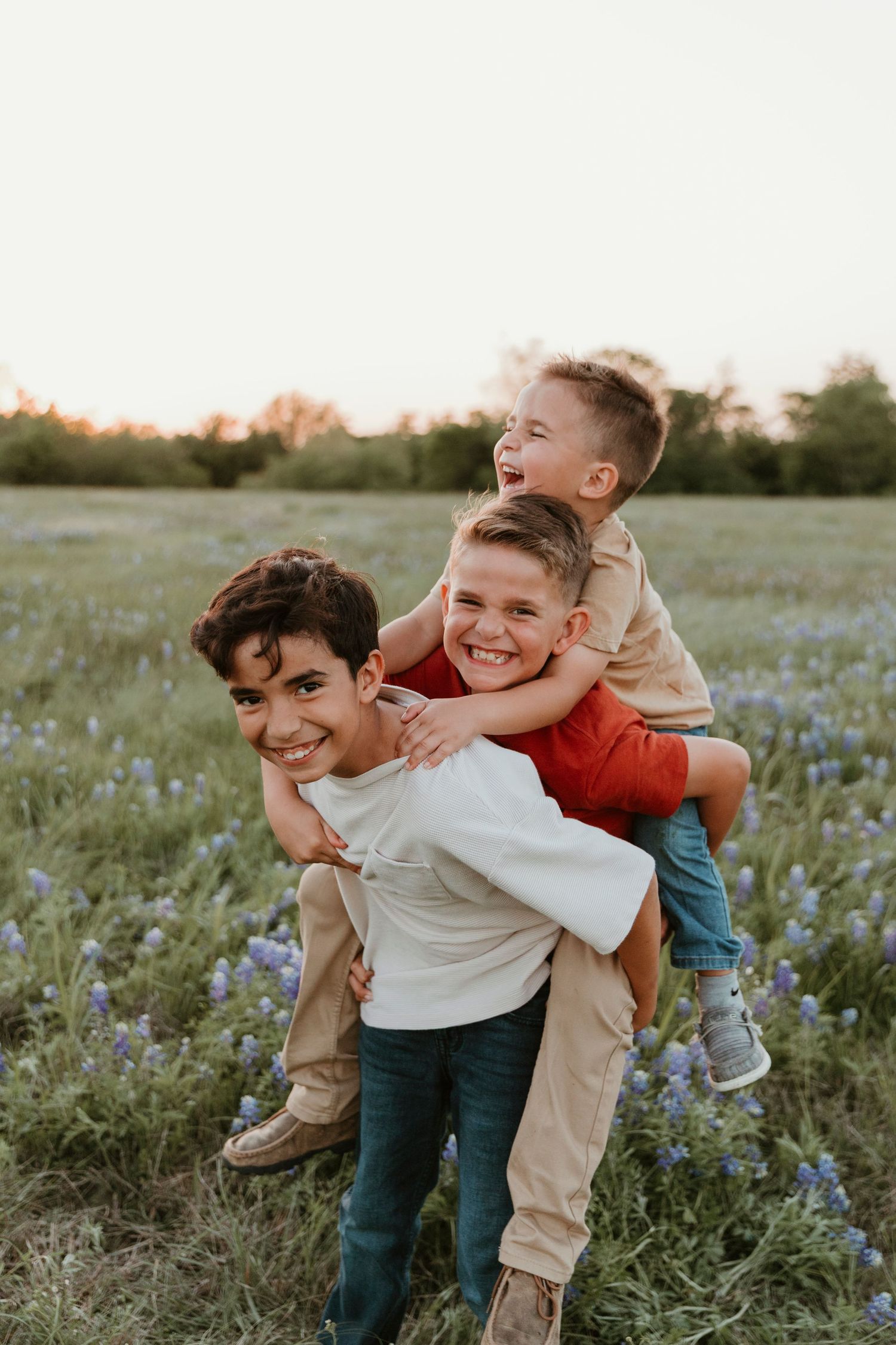 Children playing and giving piggyback rides among wildflowers in evening light.