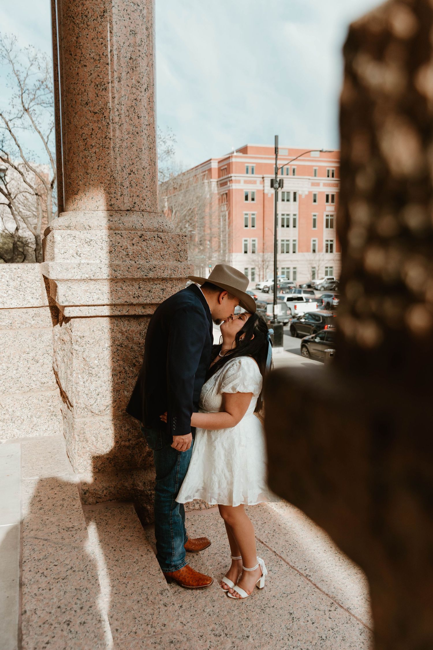 Romantic wedding photo of a couple sharing an intimate moment against a stone pillar.