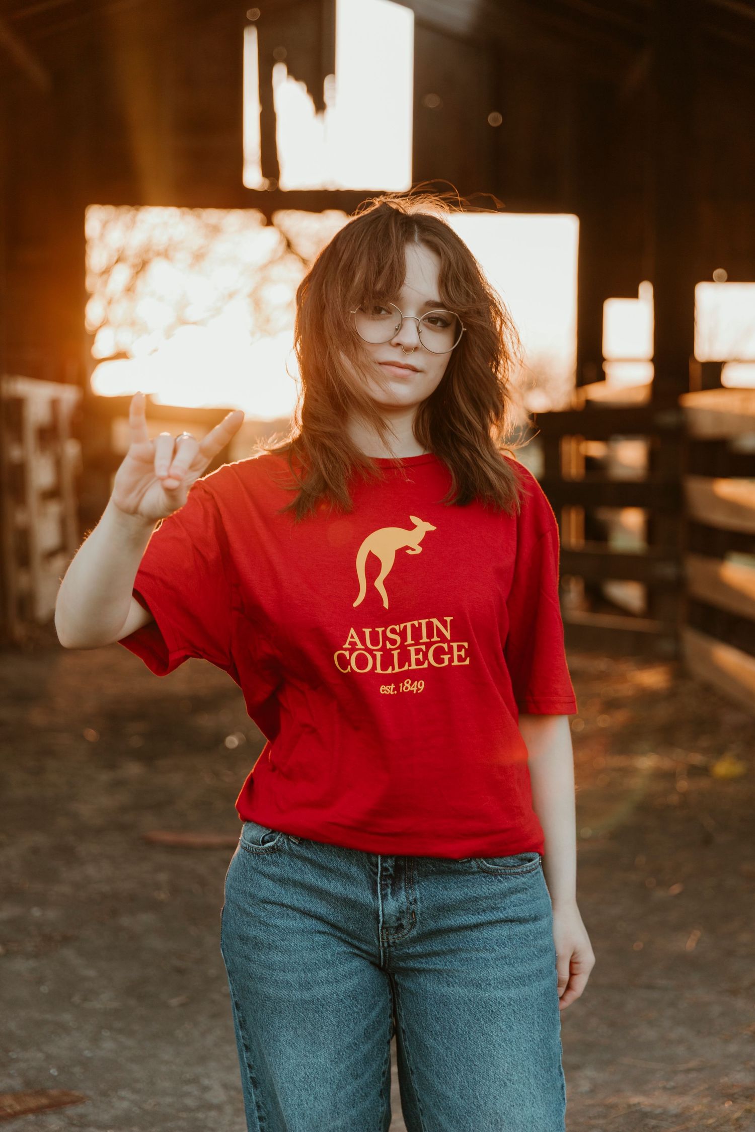 Person wearing a red college t-shirt and blue jeans poses against a dark outdoor background.