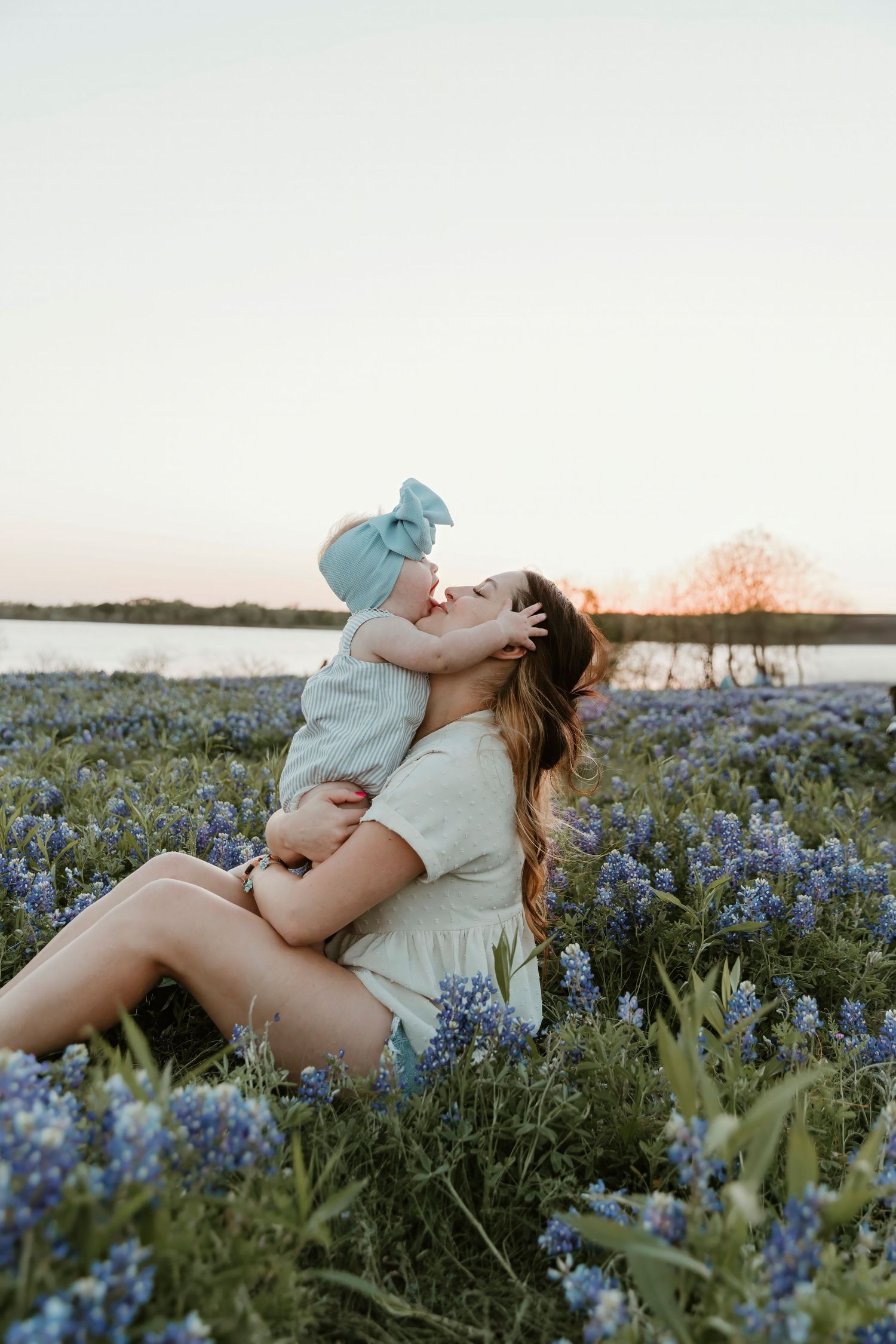 Parent lifting baby in a field of bluebonnets during sunset.