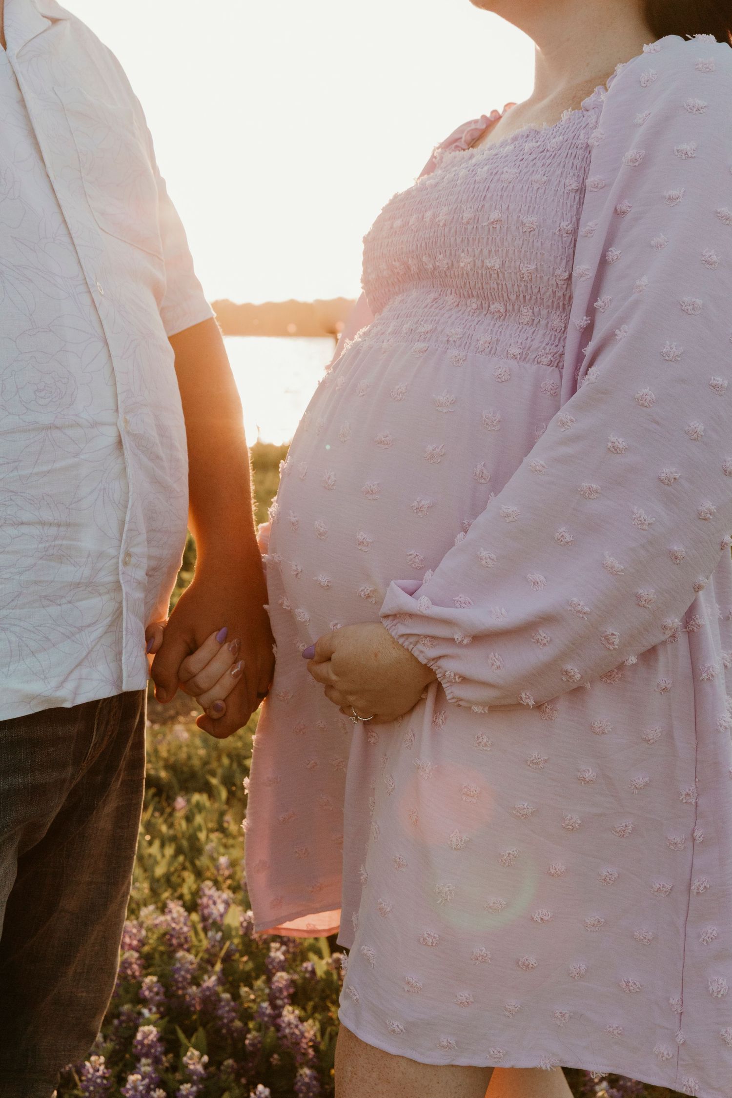 Maternity photos in soft pink dress during golden hour among wildflowers.