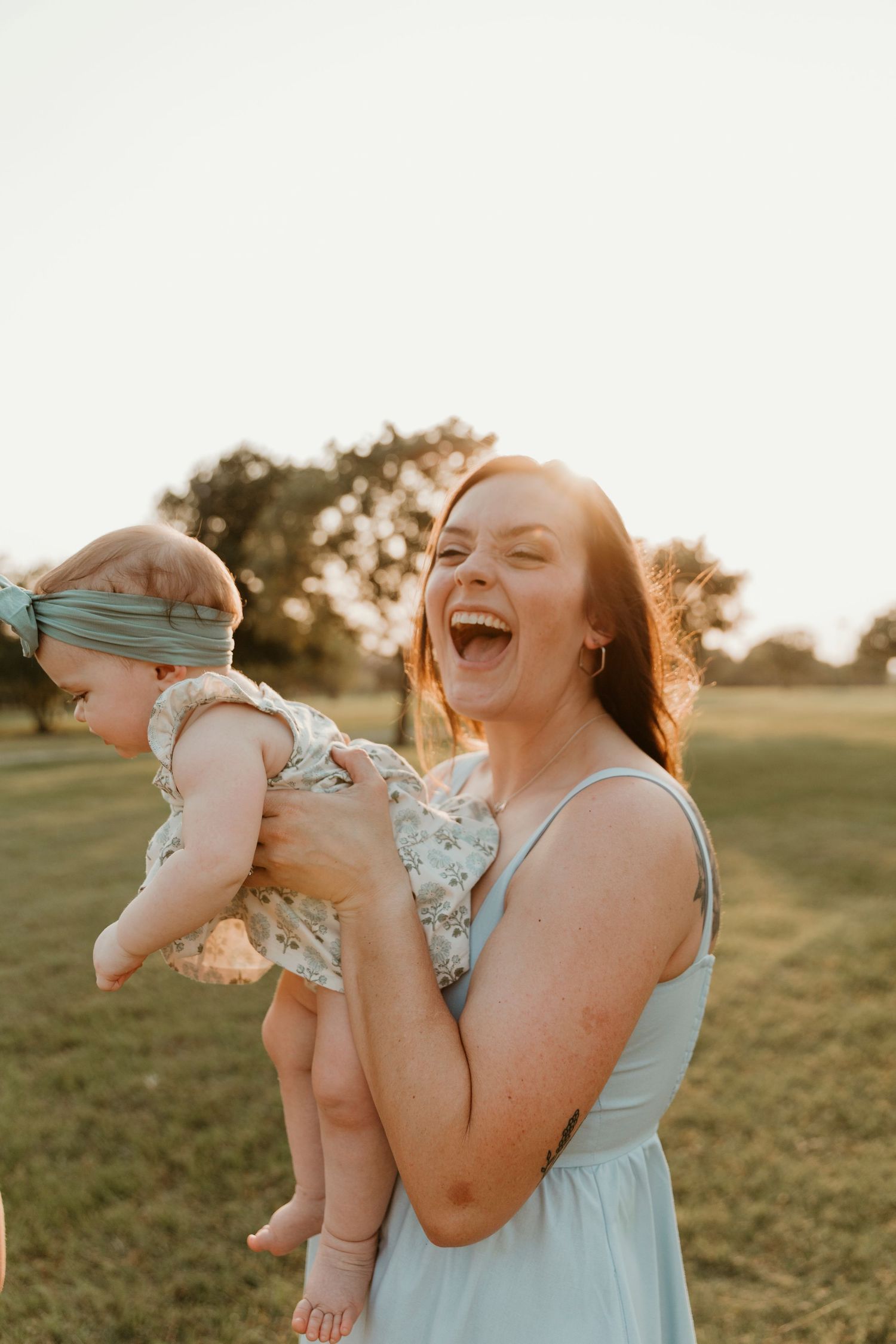 A joyful moment captured between parent and baby during golden hour in a grassy field.