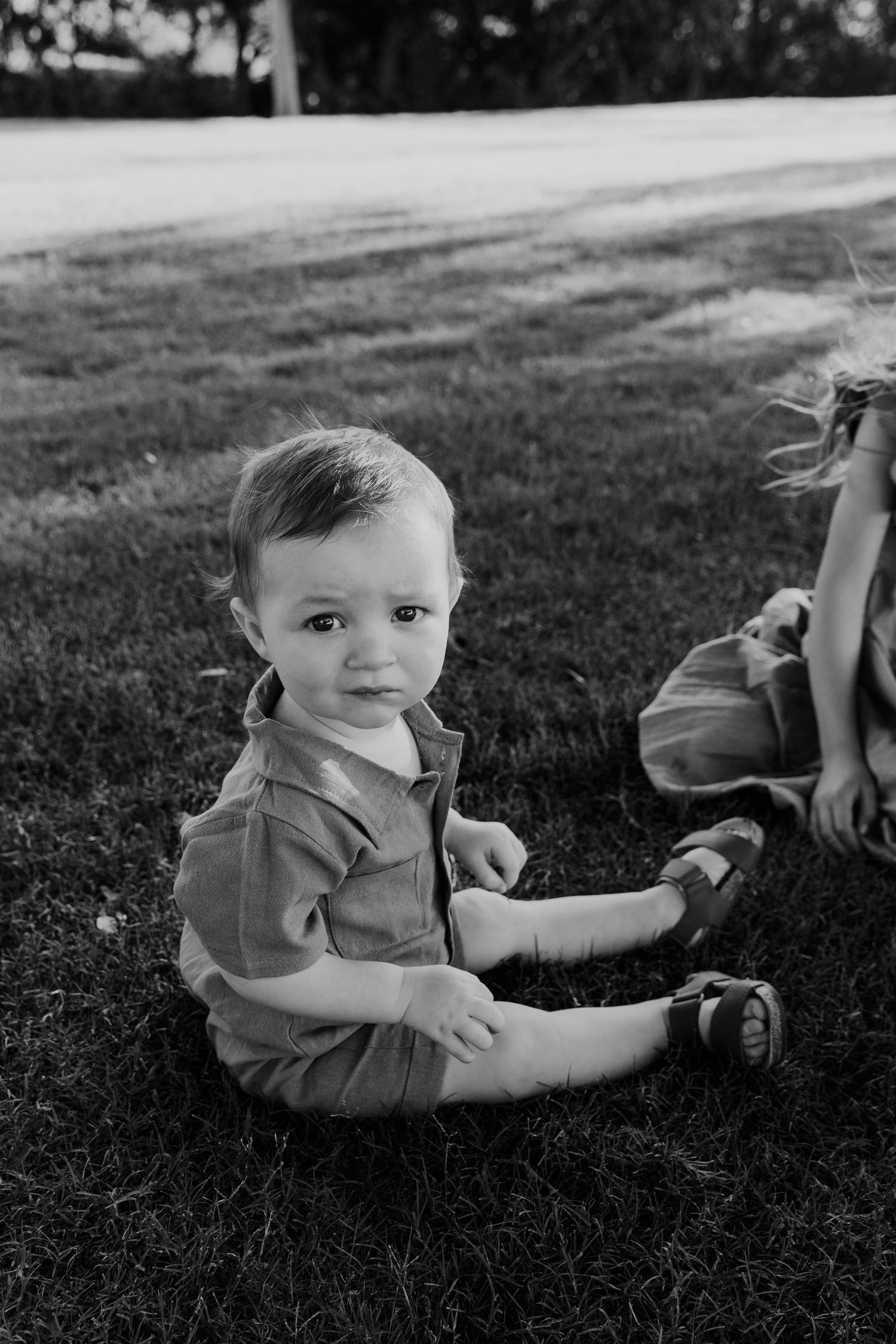 Black and white photo of a baby crawling on grass during an outdoor photoshoot.