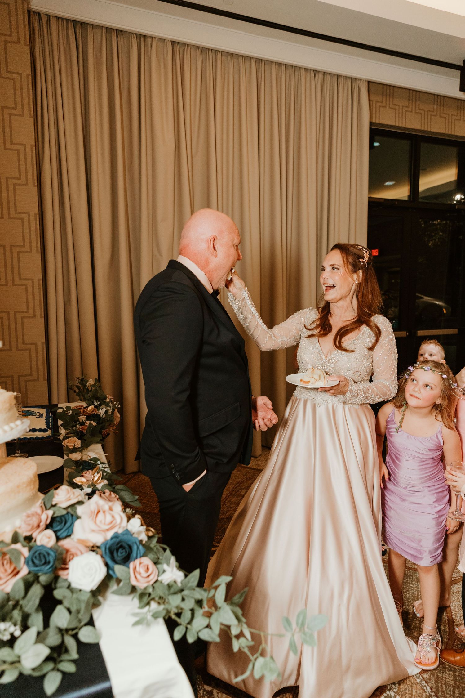 An emotional moment at a wedding reception with people in formal attire standing next to floral arrangements with blue roses.