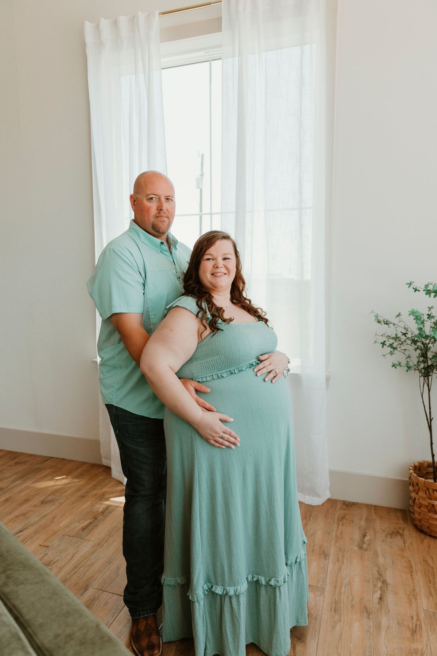 Maternity photo featuring couple in matching mint green clothing indoors.