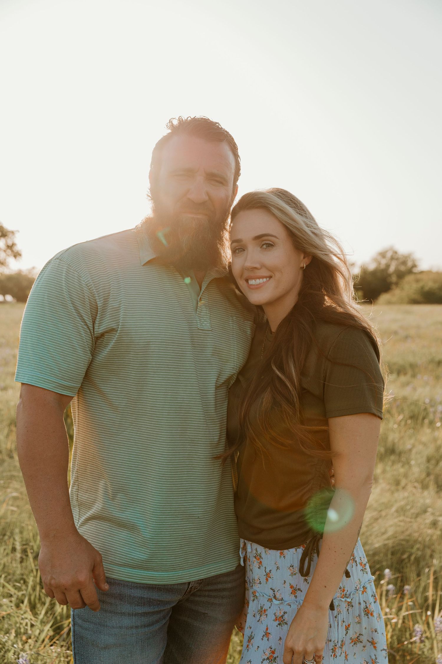 Couple poses together in a sunlit field during golden hour.