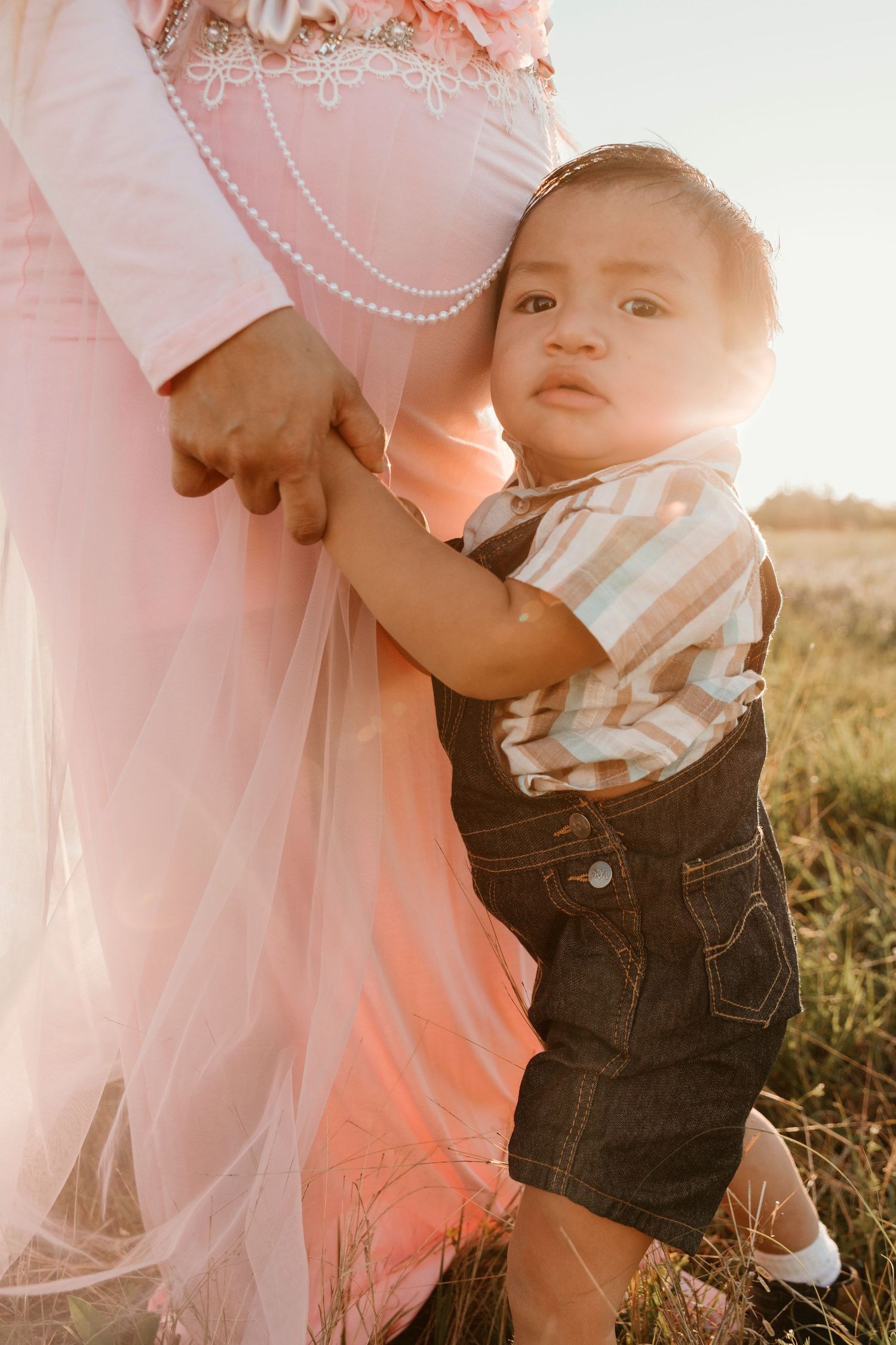 Small child in overalls holding onto a pink dress outdoors at sunset.