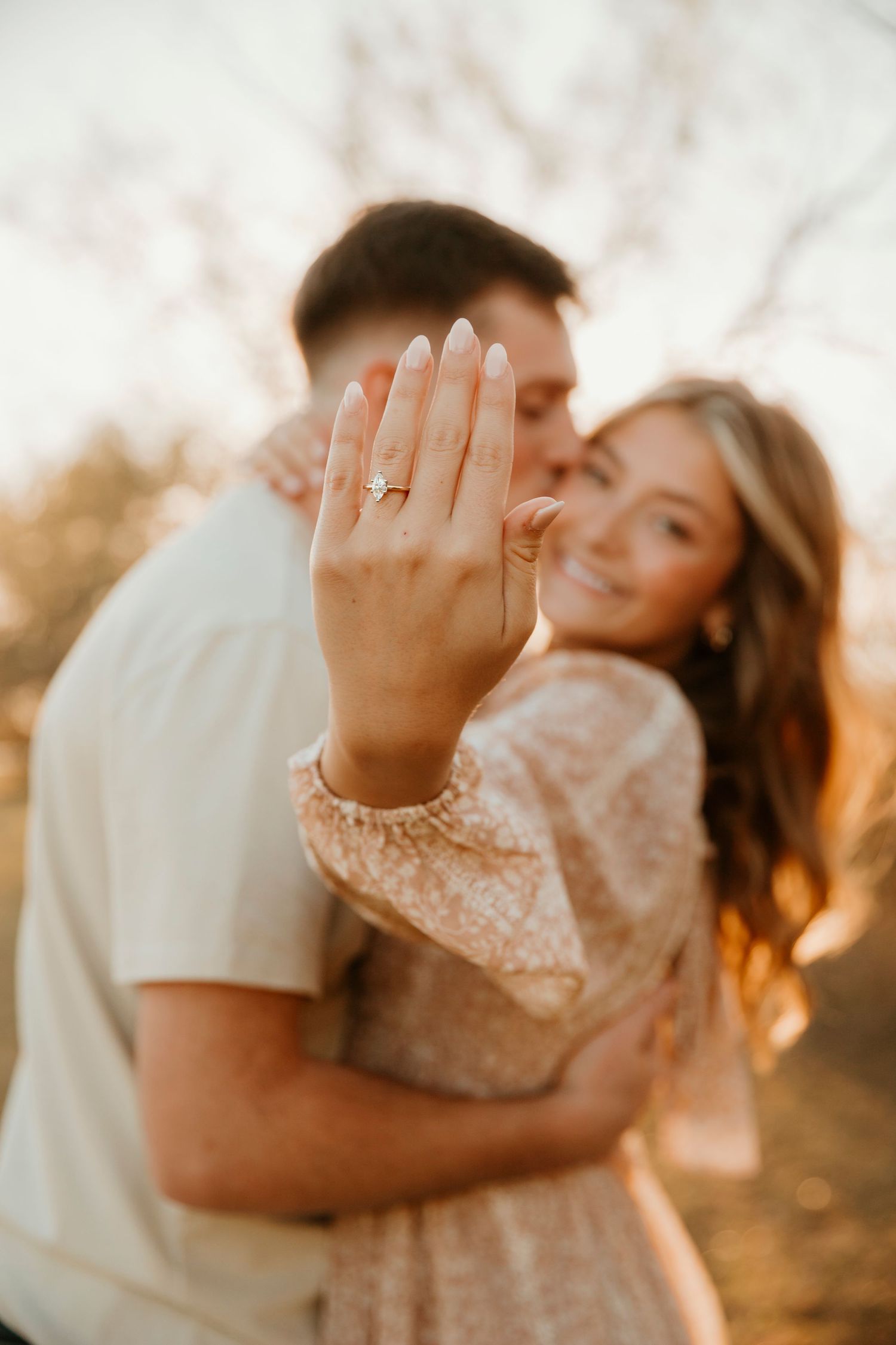 A romantic couple embraces in warm golden sunlight during a sunset photoshoot in a field.