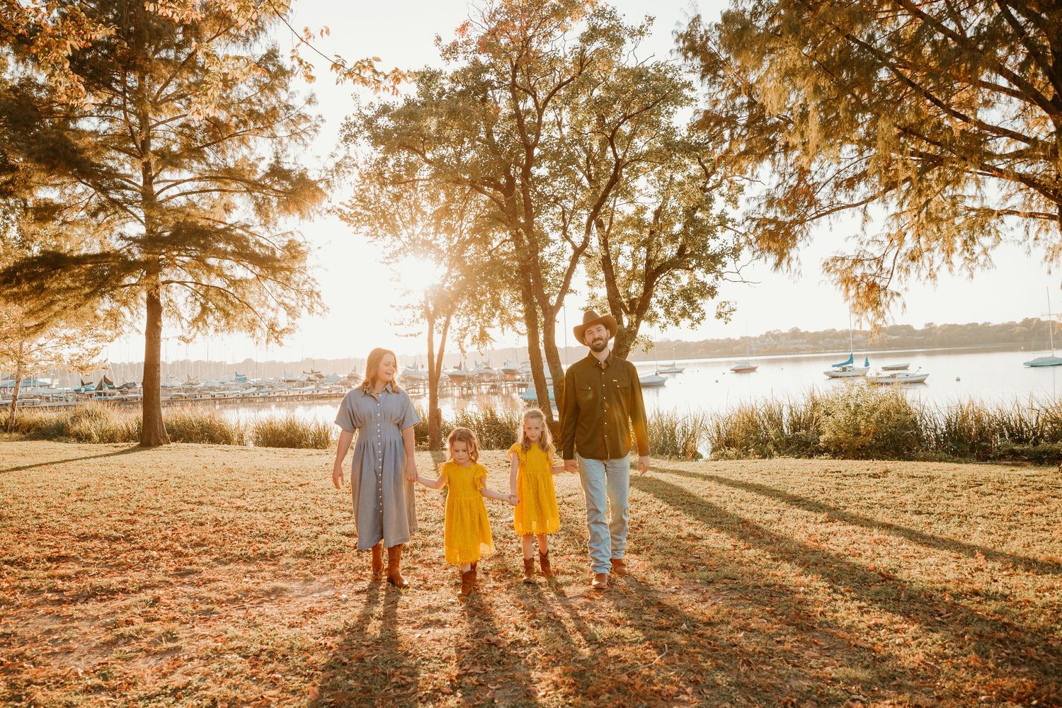 A series of silhouetted figures stand against a warm sunset backdrop with trees casting long shadows.