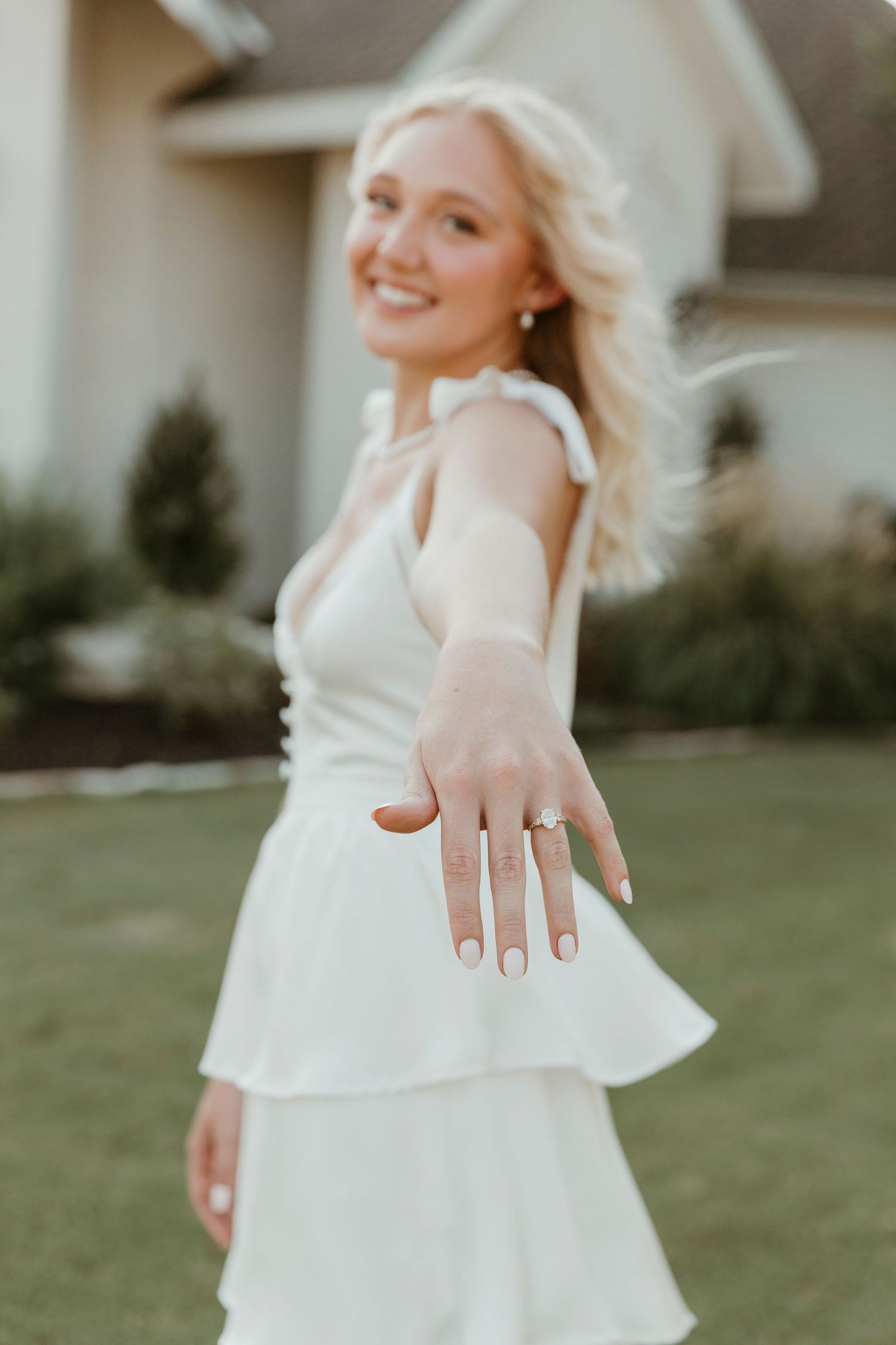 Woman in flowing white dress twirls gracefully on a grass lawn during a sunny afternoon photoshoot.