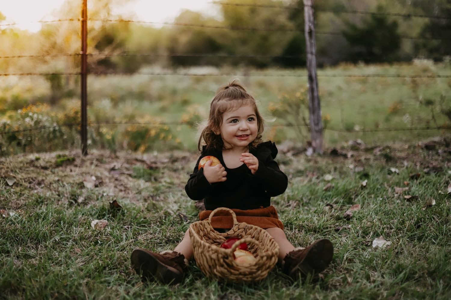 Child sitting cross-legged on grass with autumn leaves and natural lighting.