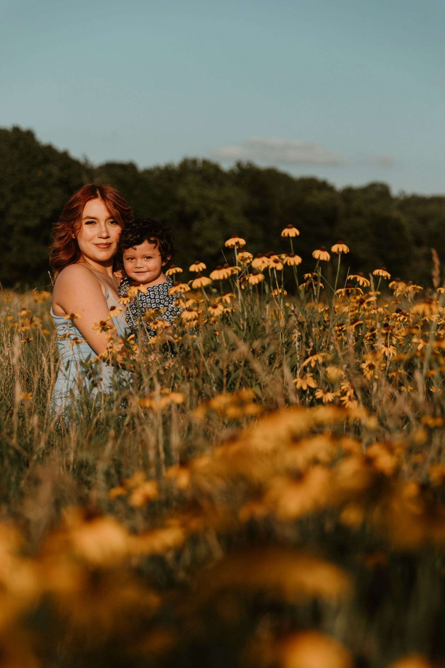 Mother and child share a tender moment in a field of yellow wildflowers during golden hour.