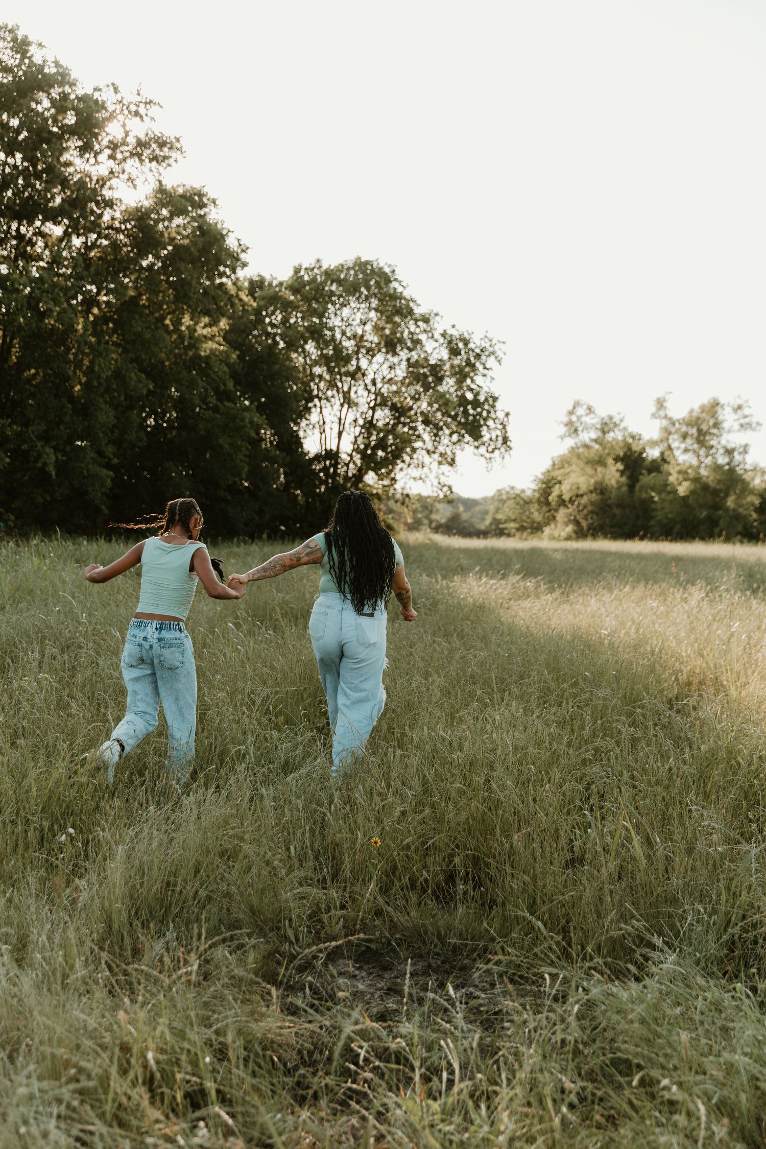Two people holding hands while running through tall grass in a sunny field.
