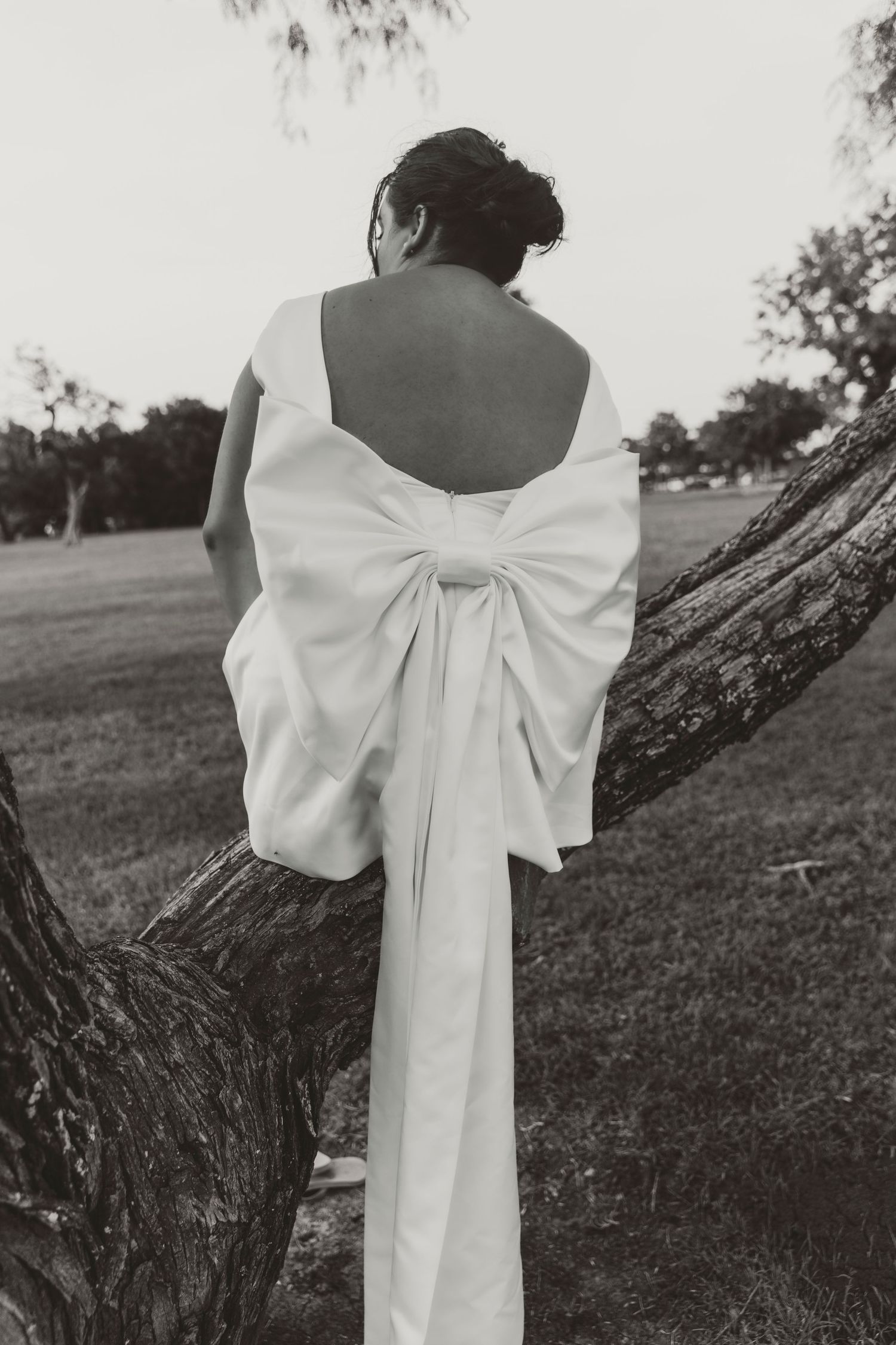 Elegant white bow detail on the back of a wedding dress set against a natural outdoor setting.
