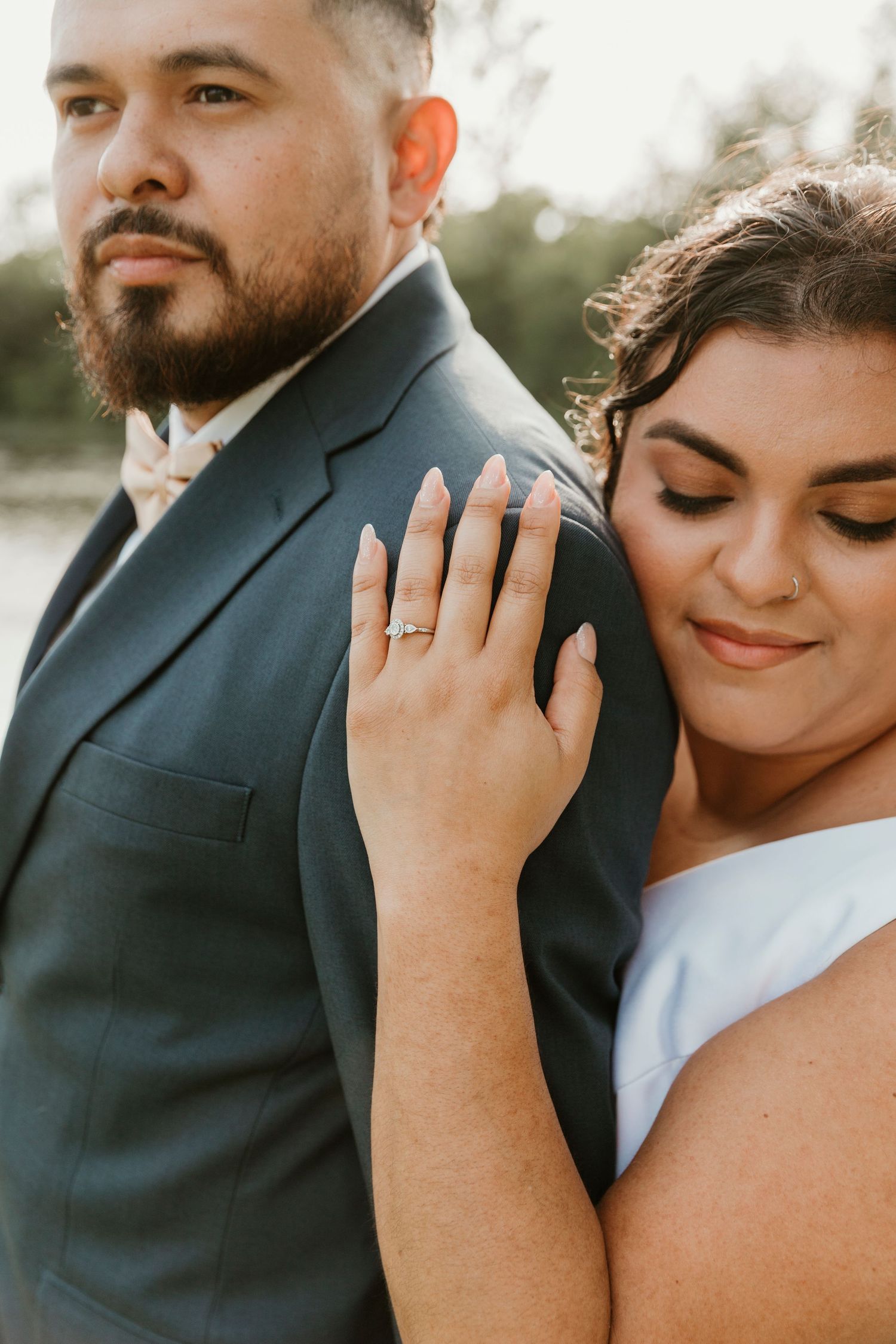 A tender wedding portrait showcasing an engagement ring as a bride embraces her groom from behind.