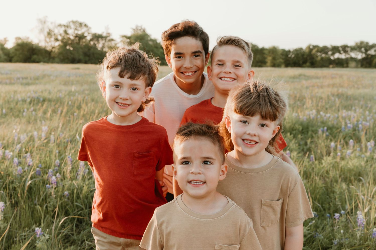 Children smiling and laughing together in a wildflower meadow during golden hour.