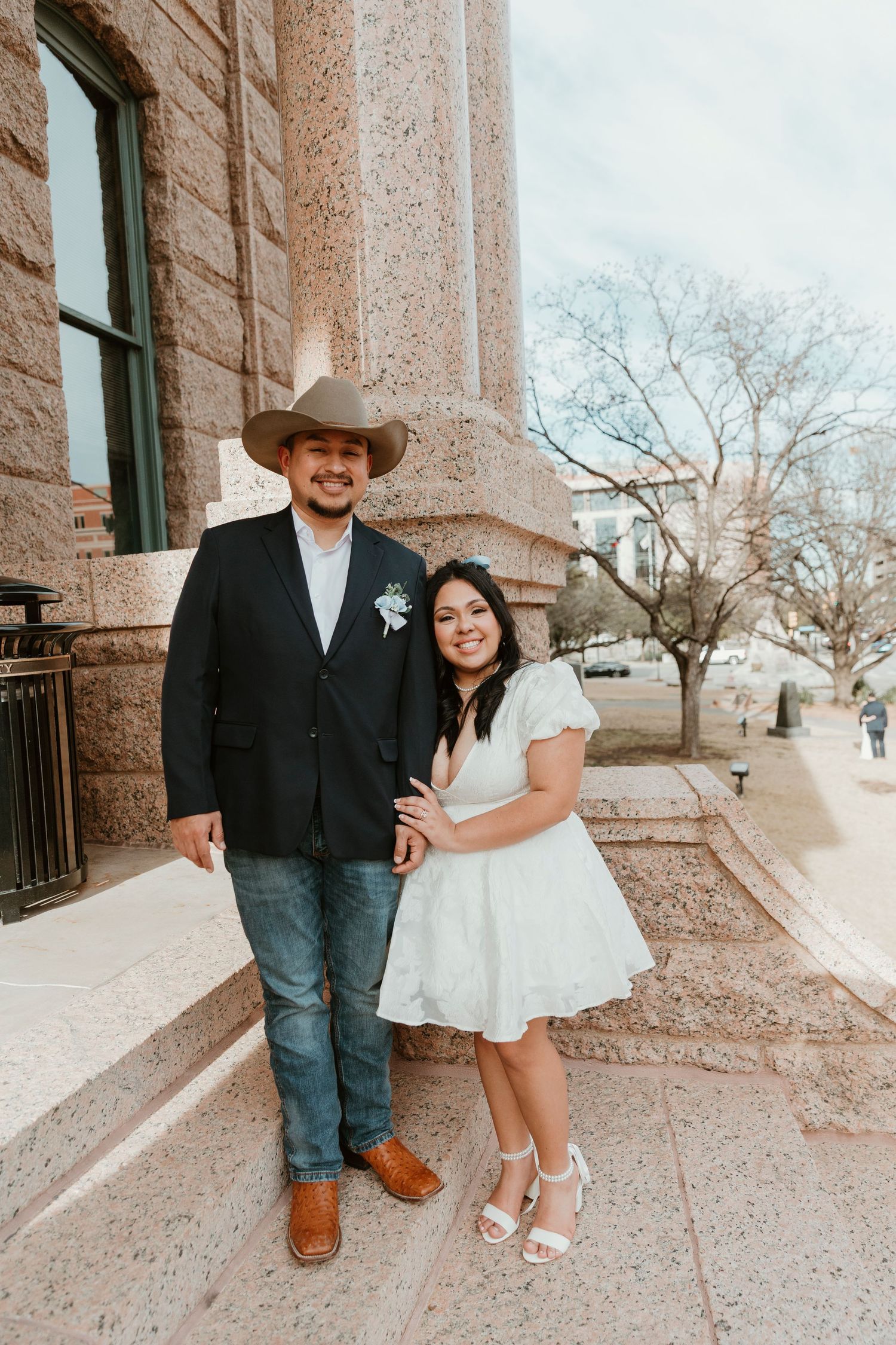 Wedding portrait of a couple outside a stone building with the groom in western attire.