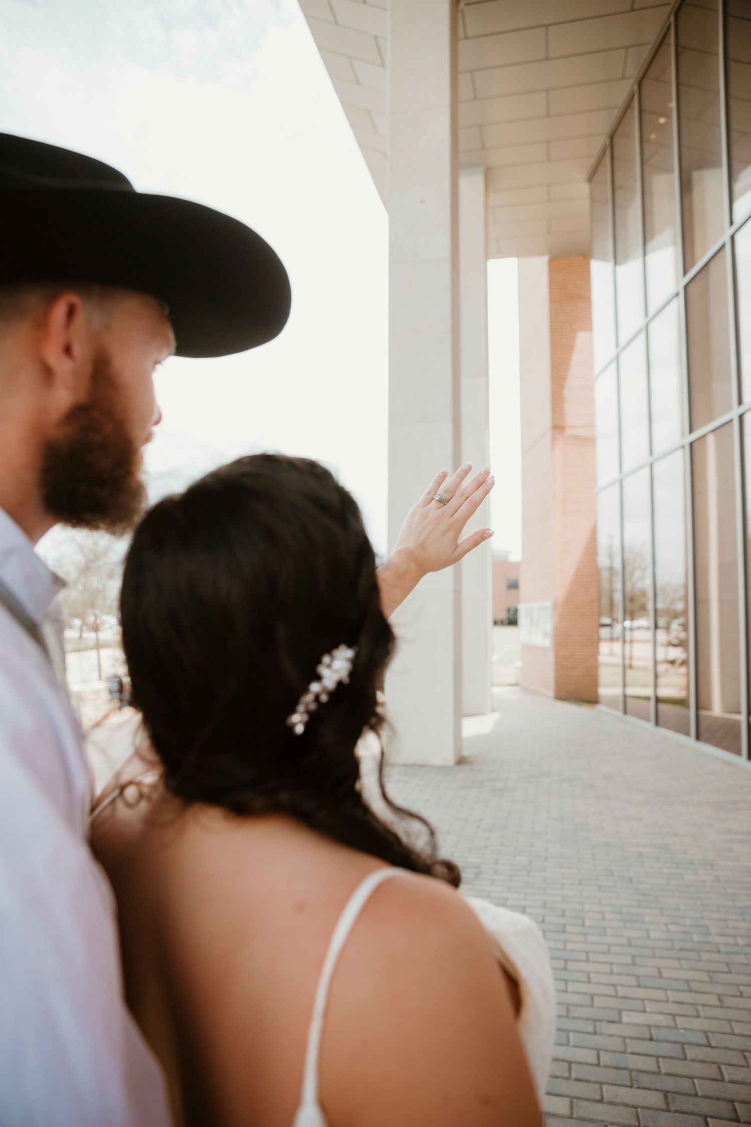 A couple stands together in a covered walkway with white columns, the bride wearing a white dress with delicate hair details.