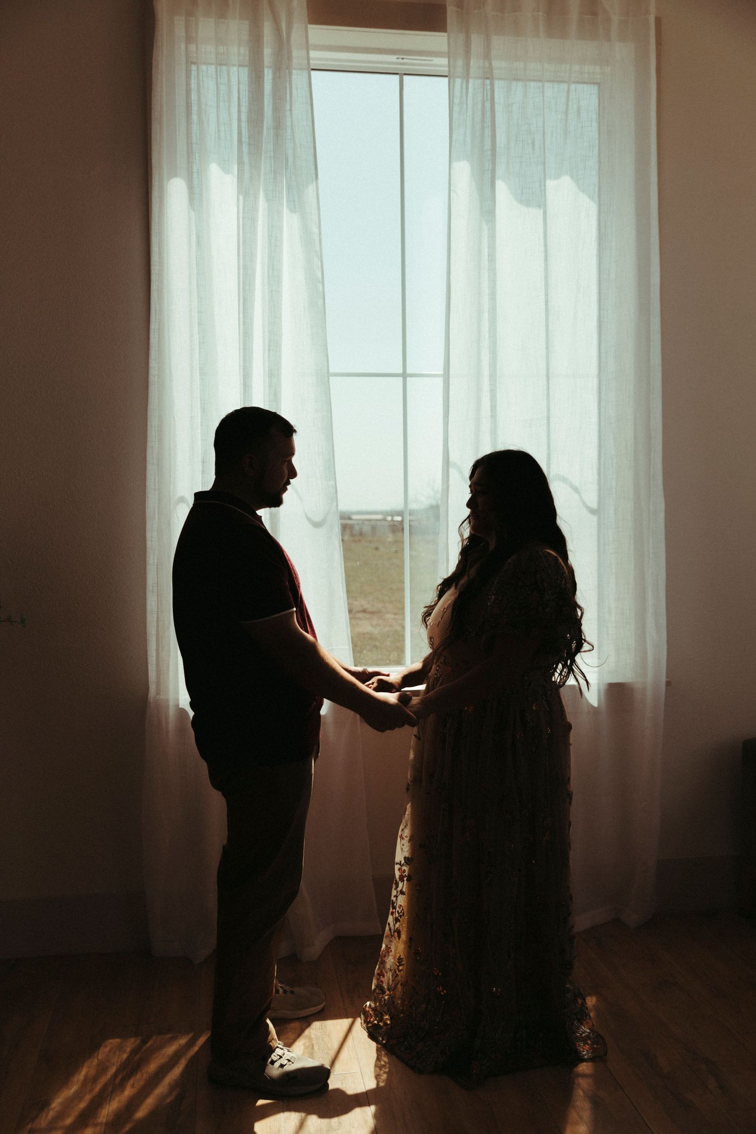 Backlit figures sharing an intimate moment by a sunlit window.