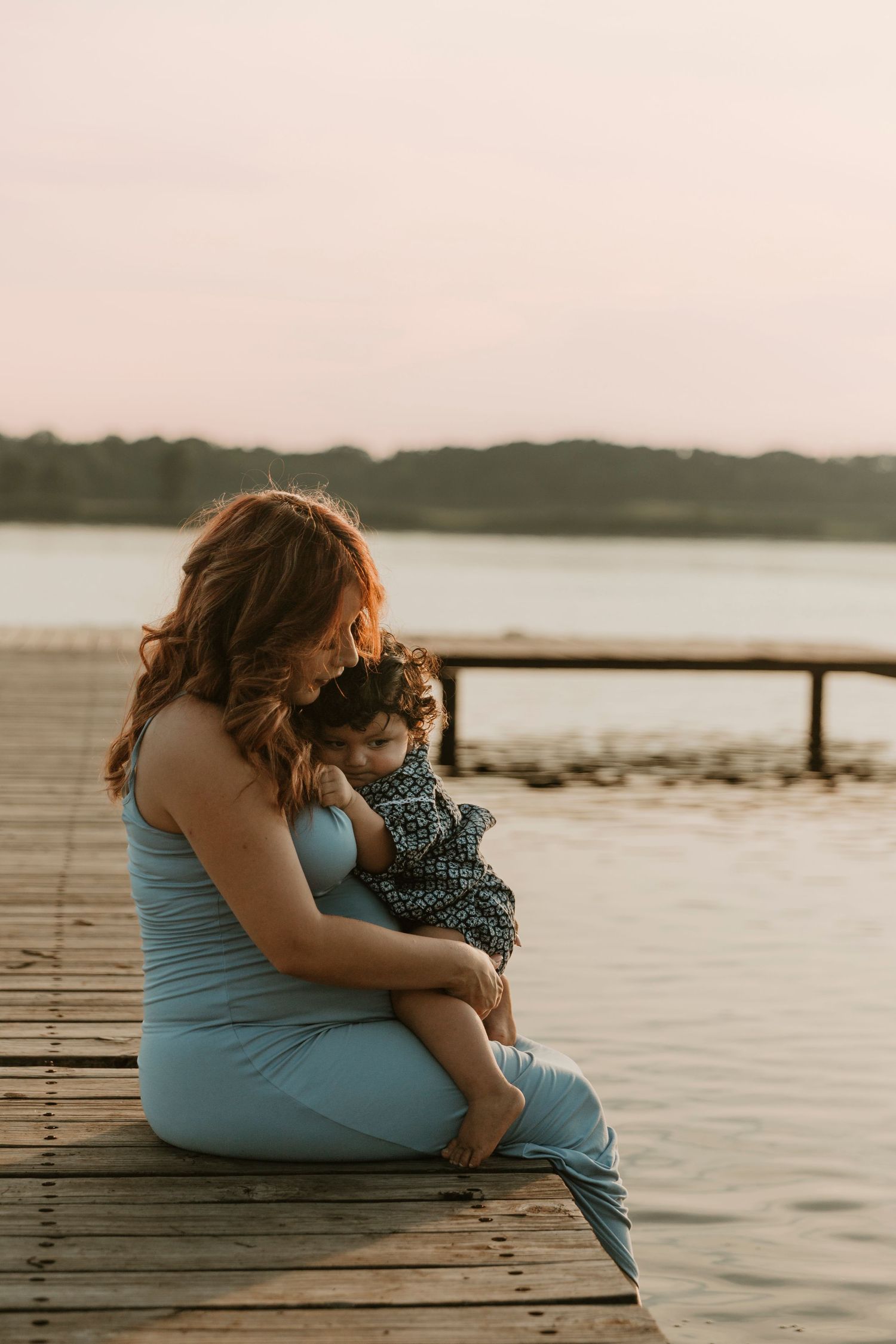 Sunset silhouette of mother and child sharing a quiet moment on a wooden dock by the water.