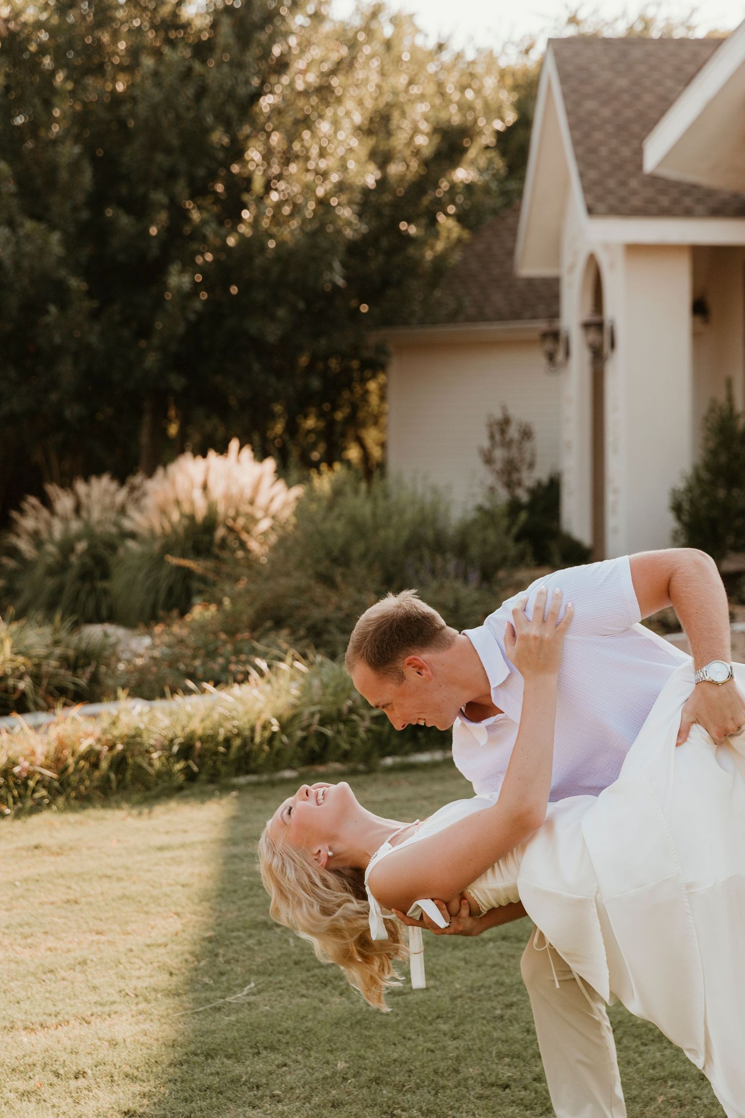 A romantic dip pose on a manicured lawn with white house and garden in the background.