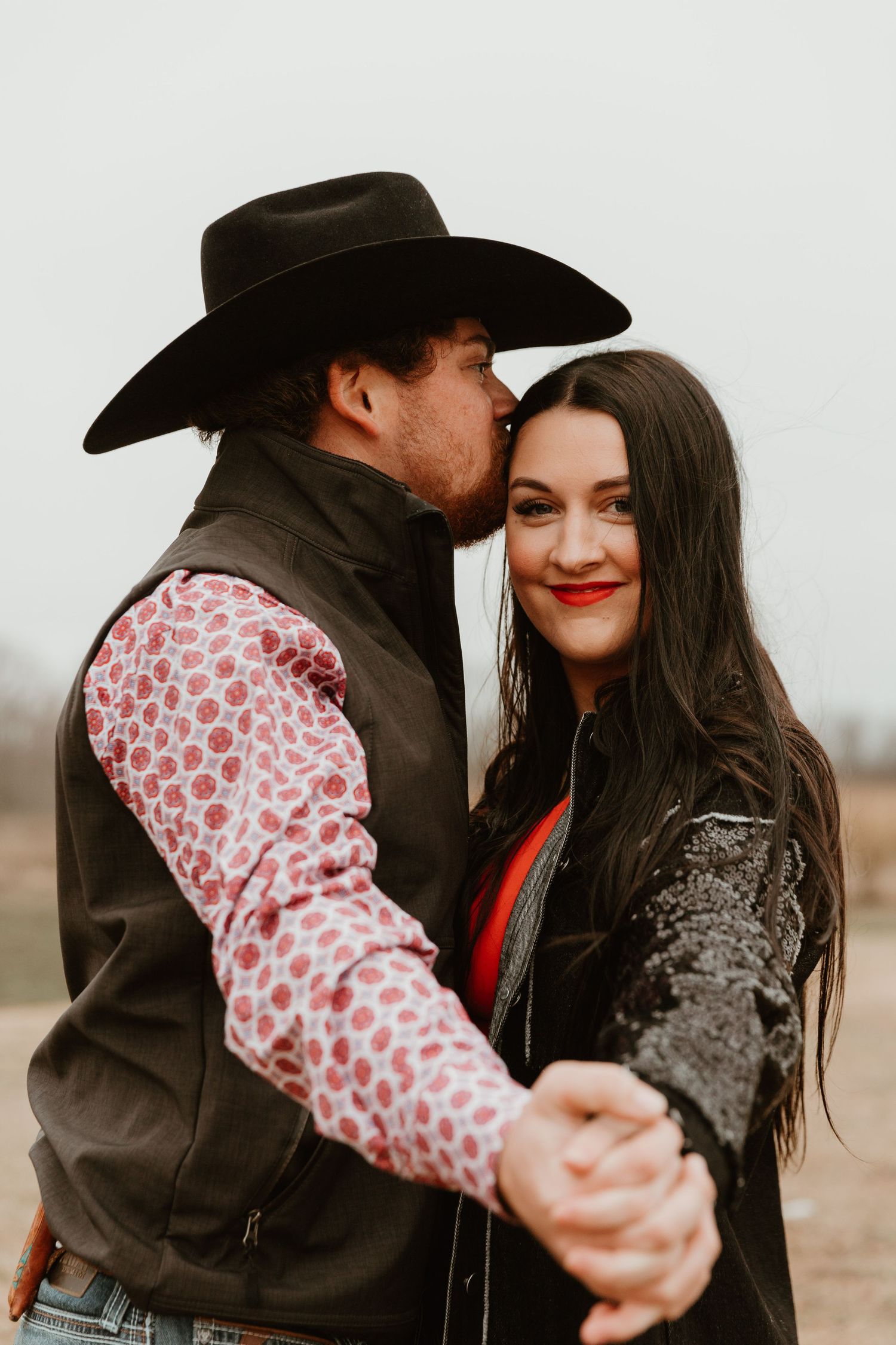 Romantic couple portrait in western attire dancing outdoors in muted winter landscape.