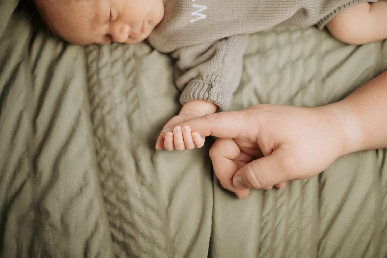 Close-up of tiny baby feet and toes being held by adult hands on textured fabric.