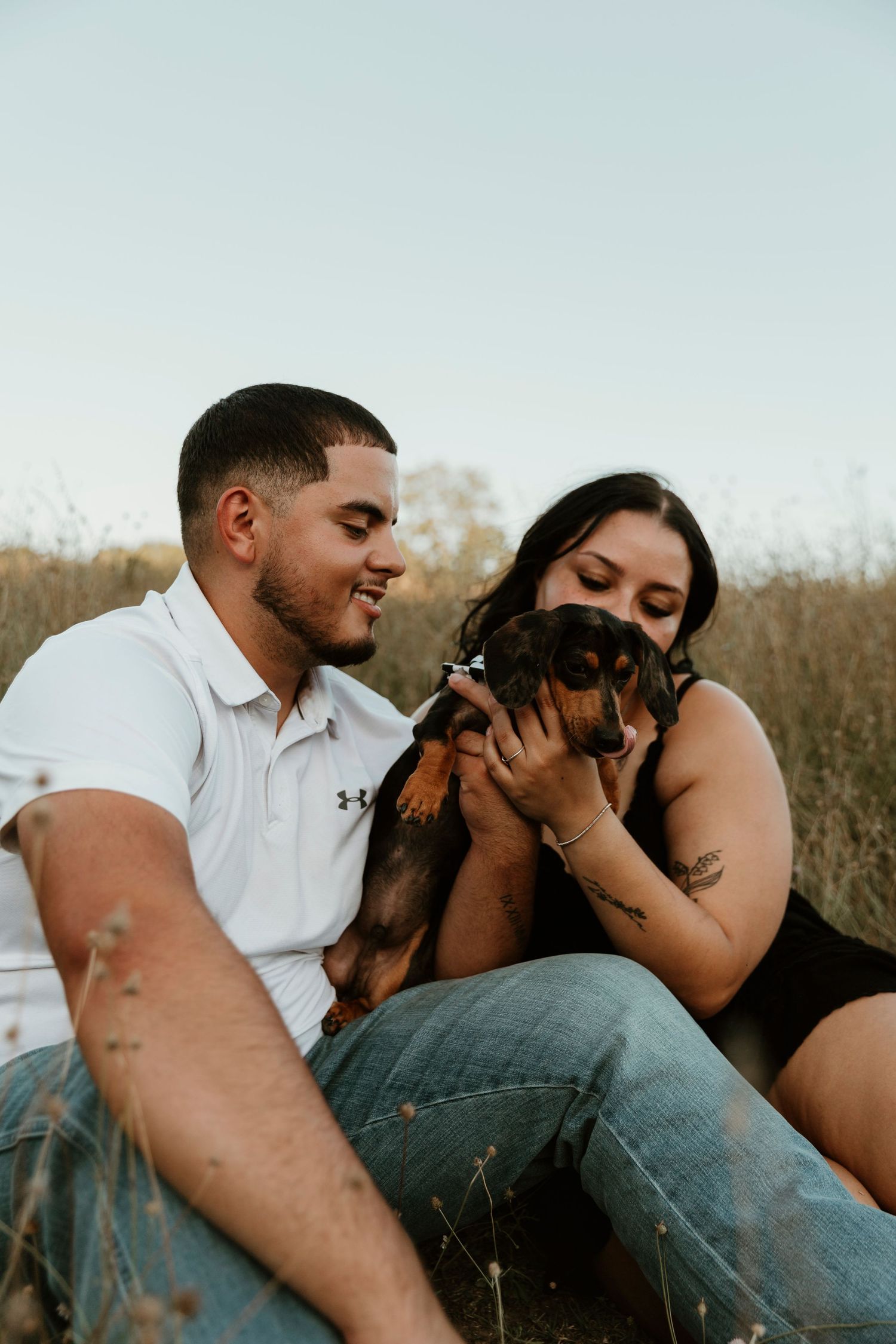 A couple relaxes in a grassy field with their German Shepherd dog on a peaceful afternoon.