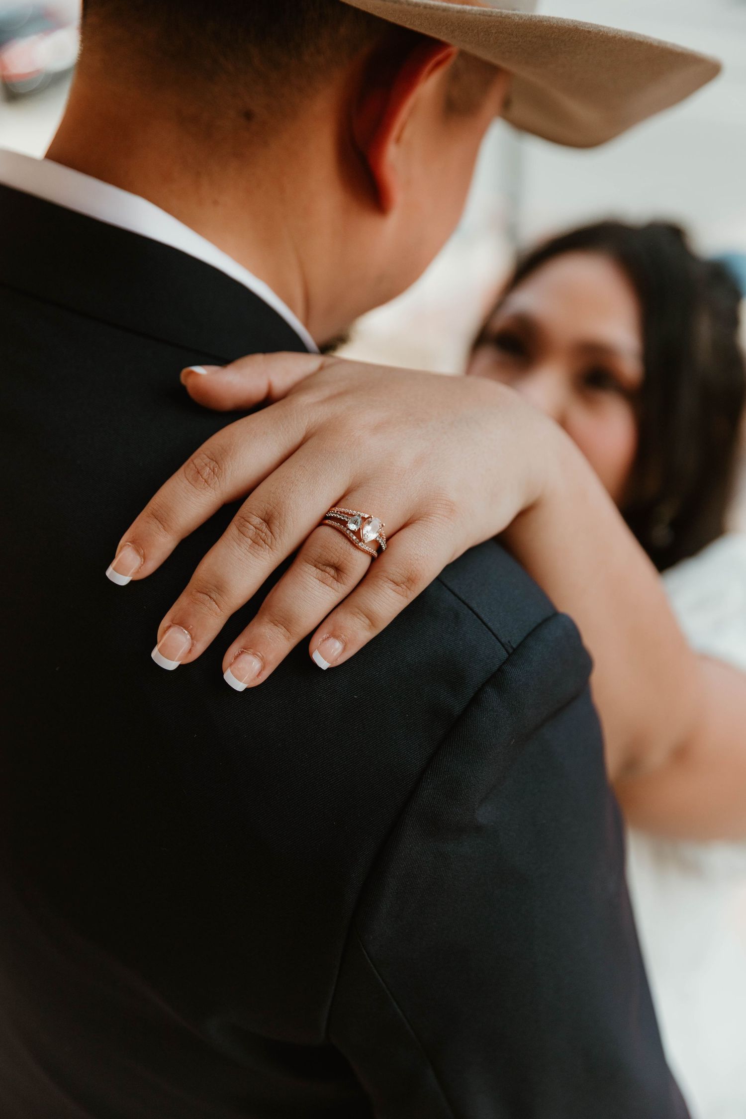 Close-up of an engagement ring on hand resting against formal attire.