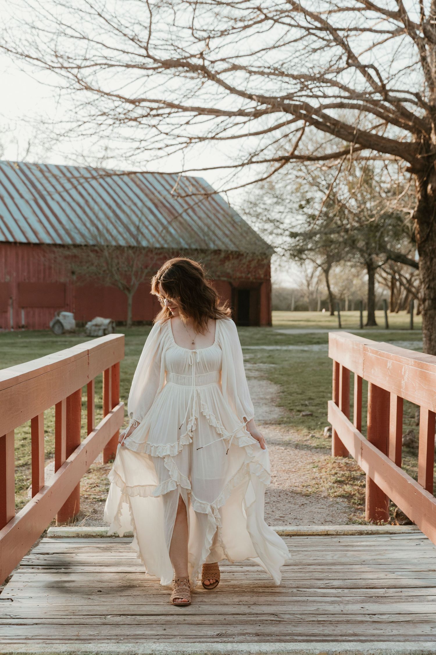 A flowing white dress captured on a wooden bridge with a red barn in the background.